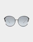 The Alectrona by For Art's Sake® are round sunglasses featuring thin black frames, slightly tinted grey nylon lenses, and decorative curved accents on the top outer corners. The UVA & UVB-protected lenses promise superior defense. The background is plain white.

