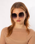 A person with shoulder-length, light brown hair is wearing the Generation sunglasses by For Art's Sake®. They are dressed in a sheer beige top and are facing the camera with a neutral expression against a plain, light-colored background.