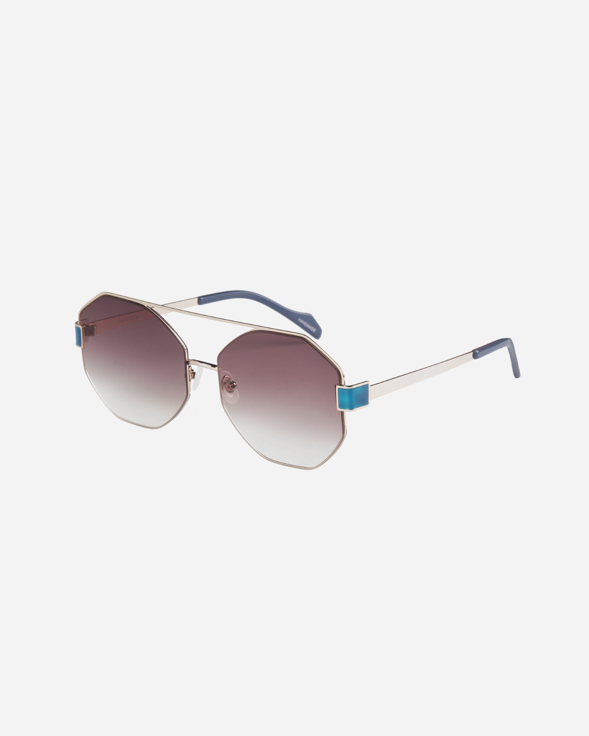 A pair of For Art's Sake® Mania sunglasses with stainless steel, hexagonal frames and gradient nylon lenses that transition from dark at the top to lighter at the bottom. The temples are thin with blue tips. The adjustable nosepads are small and clear for comfort.