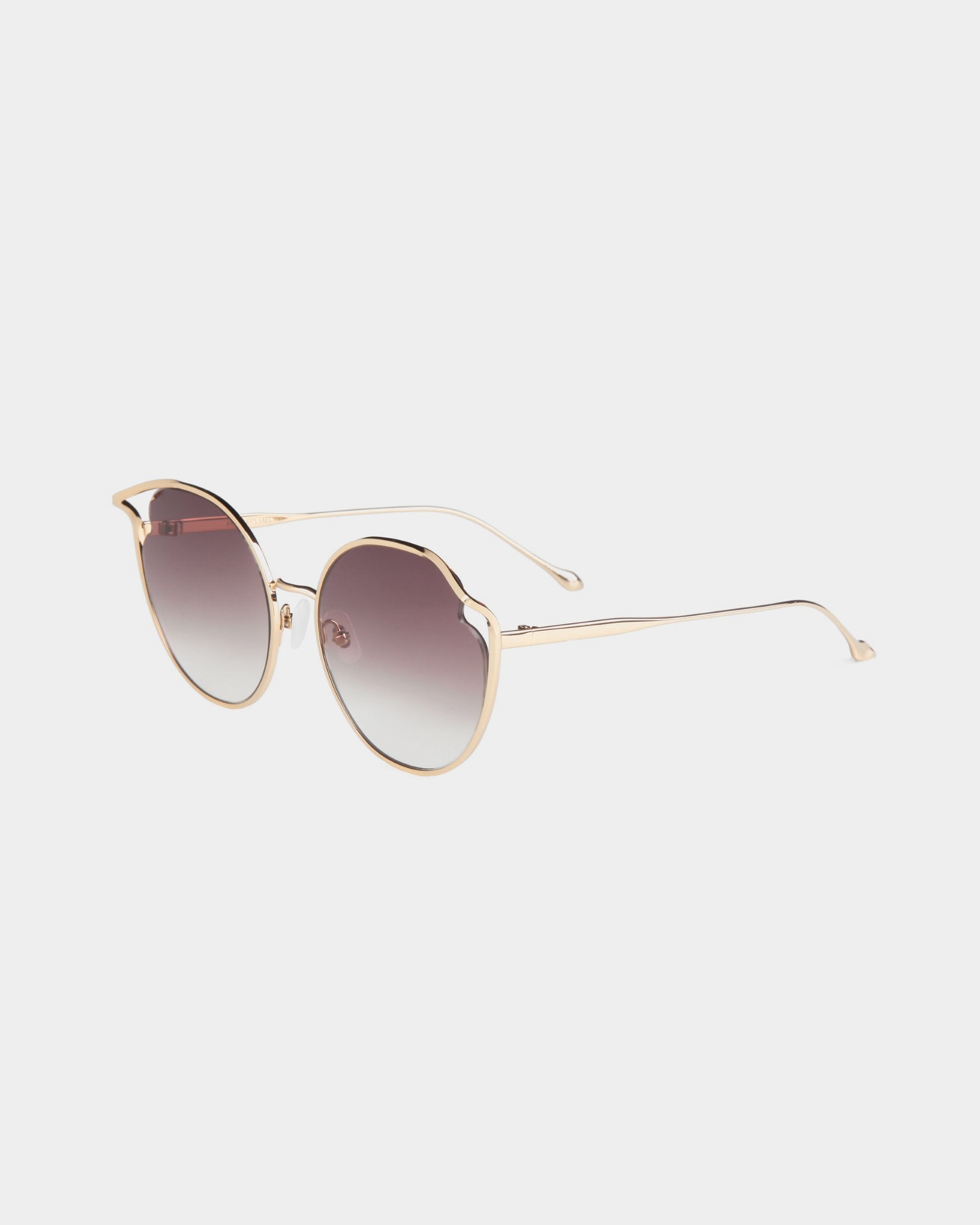 An image of the stylish Cat sunglasses by For Art&#39;s Sake®, featuring round, gradient Nylon lenses and a sleek, gold-colored frame. The gradient lenses transition from dark to light and are UVA &amp; UVB-protected. The frame boasts thin, elegant arms with curved tips and adjustable nosepads for added comfort. The design is modern and minimalist.