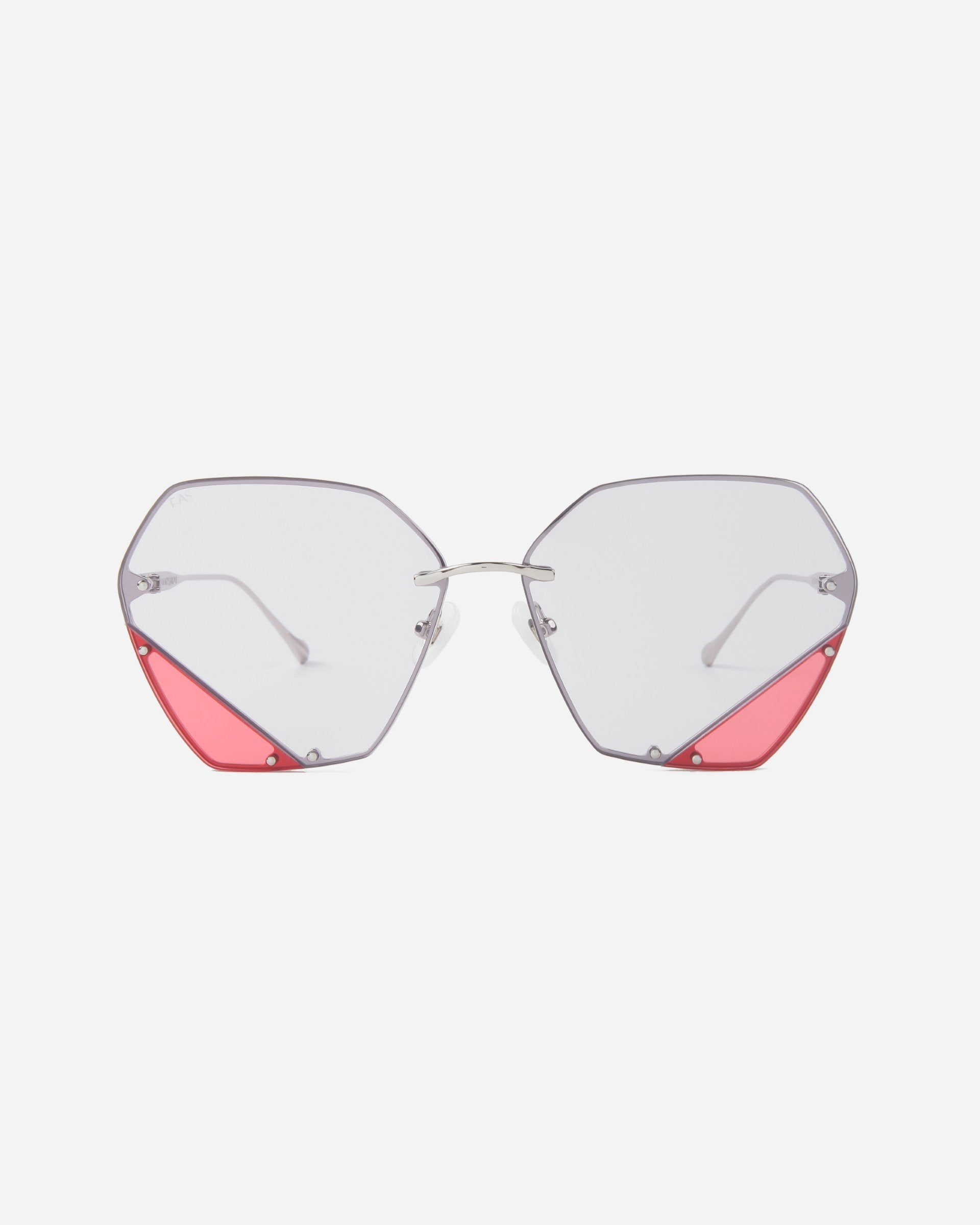 A pair of stylish eyeglasses with UV protection, featuring octagonal clear lenses and silver frames. The bottom corners of the geometric lenses boast pink triangular accents, adding a pop of color to the otherwise minimalist design. The added touch of jadestone nosepads enhances comfort and elegance. These are the Icy by For Art&#39;s Sake®.