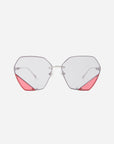 A pair of stylish eyeglasses with UV protection, featuring octagonal clear lenses and silver frames. The bottom corners of the geometric lenses boast pink triangular accents, adding a pop of color to the otherwise minimalist design. The added touch of jadestone nosepads enhances comfort and elegance. These are the Icy by For Art's Sake®.