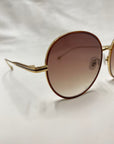 Close-up of the For Art's Sake® Lemon sunglasses featuring round, brown gradient lenses and thin, 18-karat gold frames. The background is a plain white surface.