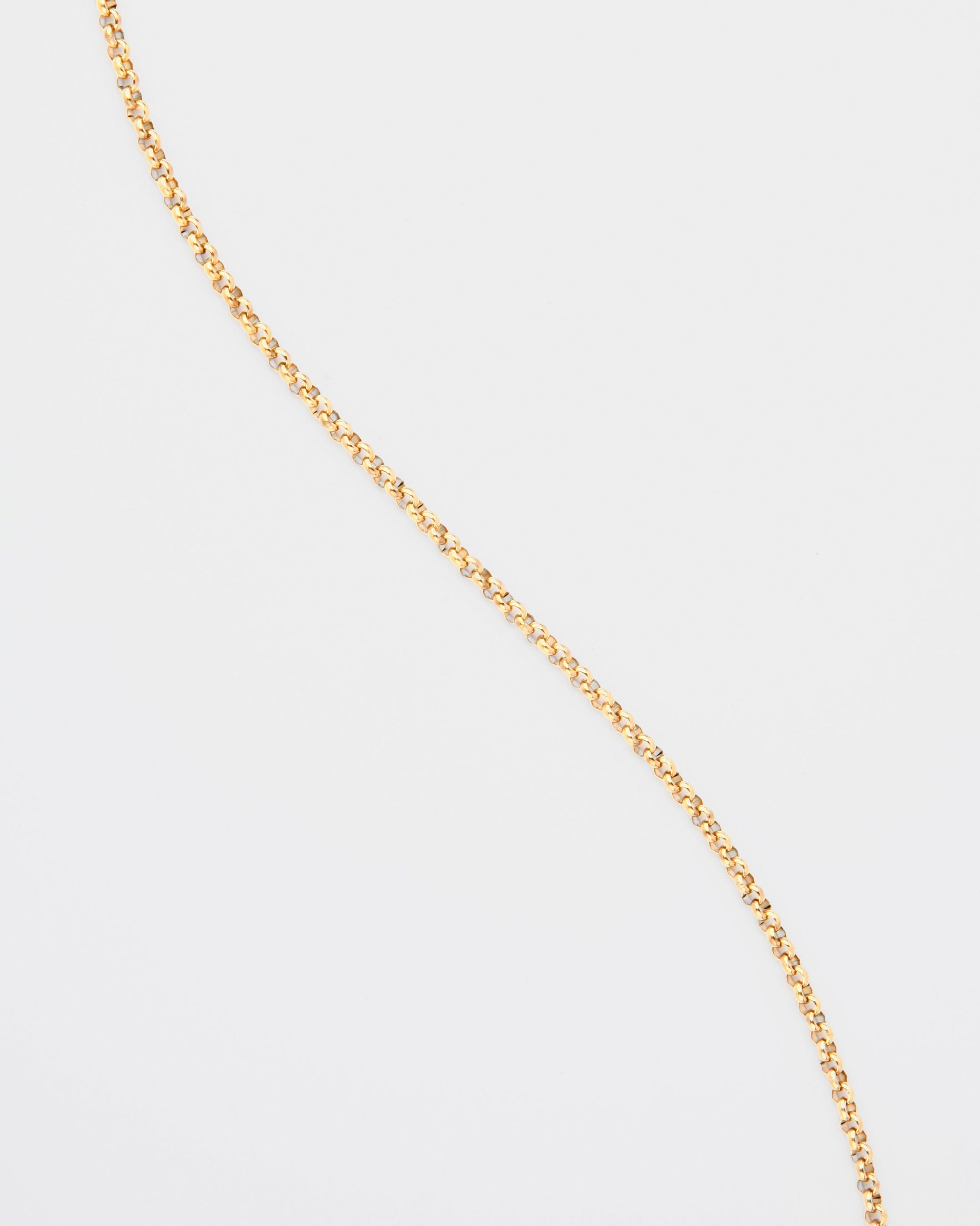A thin, 18K gold-plated chain with small, round links is draped diagonally across a plain white background. The Florentina Glasses Chain by For Art&#39;s Sake® is simple and elegant with a slight shine.