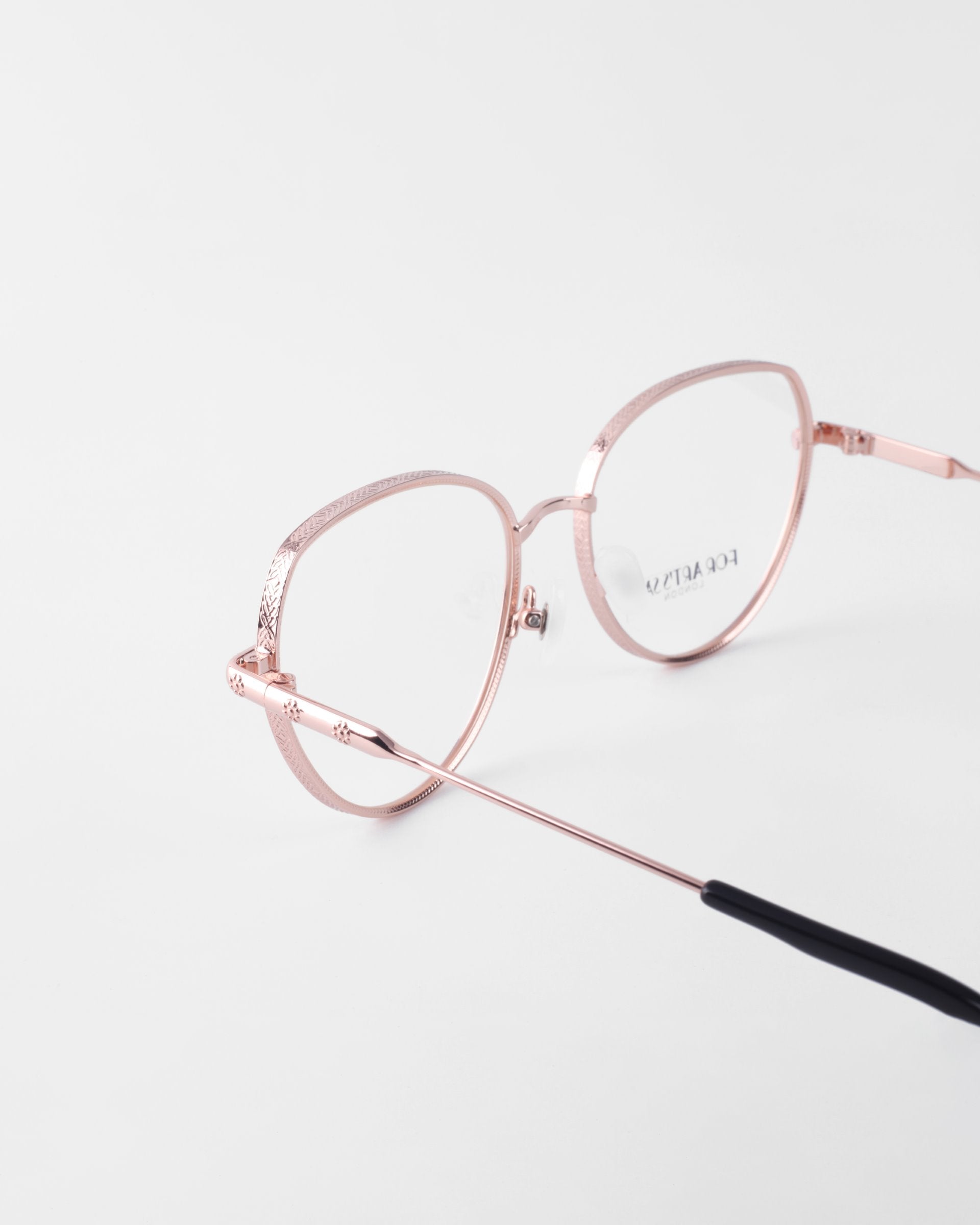 A pair of rose gold wireframe eyeglasses with a rounded shape and thin temples featuring black tips. The 18-karat gold-plated frames are equipped with prescription lenses, enhancing the minimalist and elegant design against a white background. For Art’s Sake®&#39;s Frida Floral eyeglasses effortlessly combine style and function for a timeless look.