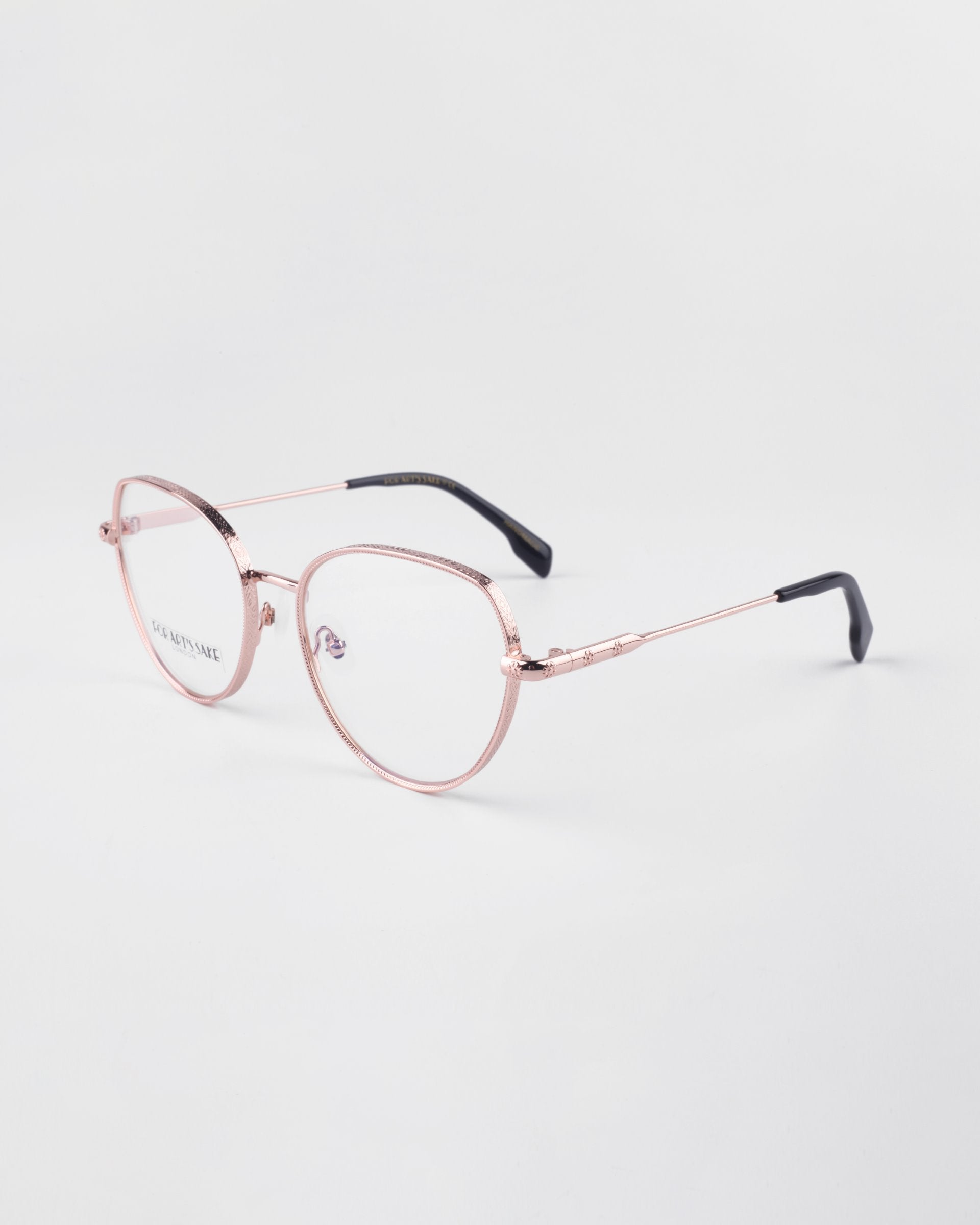 A pair of round, 18-karat gold-plated eyeglasses with a light pink tint. The **Frida Floral** glasses by **For Art&#39;s Sake®** have thin frames with nose pads and black tips at the ends of the temples, featuring blue light filter lenses. They are placed on a simple, white background.