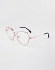 A pair of round, 18-karat gold-plated eyeglasses with a light pink tint. The **Frida Floral** glasses by **For Art's Sake®** have thin frames with nose pads and black tips at the ends of the temples, featuring blue light filter lenses. They are placed on a simple, white background.