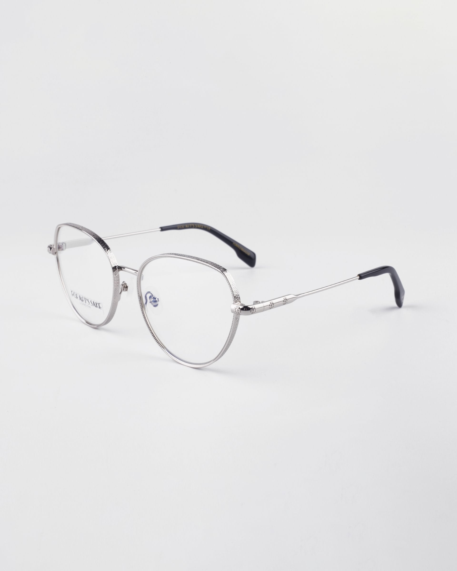 A pair of stylish round metal eyeglasses with a silver, 18-karat gold-plated frame and black temple tips, placed on a white background. The Frida Floral by For Art&#39;s Sake® glasses have thin, delicate frames and nose pads for comfort. Complete with blue light filter for extra eye protection.