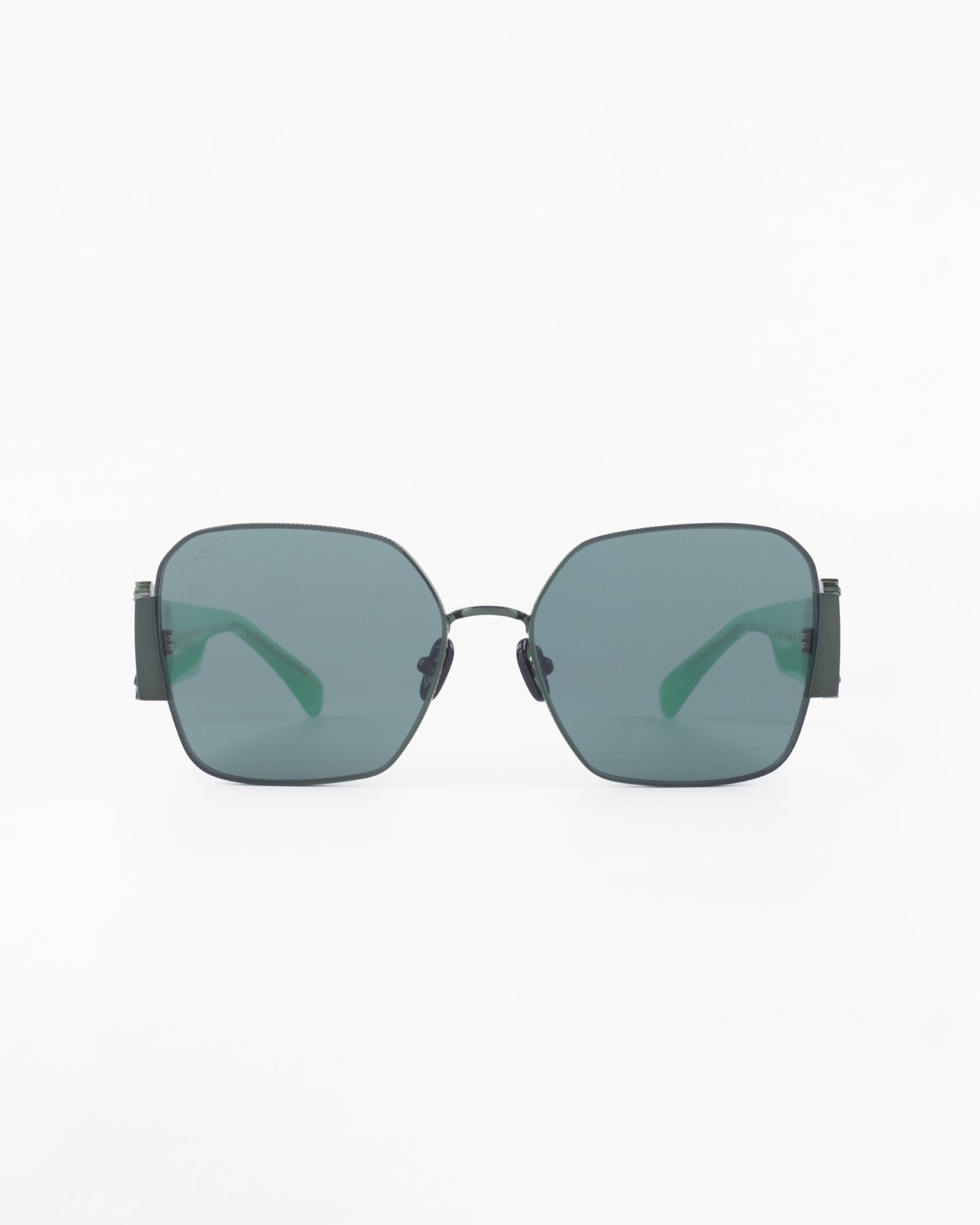 A pair of stylish, modern Frida Mask sunglasses from For Art&#39;s Sake® with black metal frames and dark green-tinted square lenses. The design features thin temples that curve inward slightly towards the ends, contrasting against the clear background. The ultra-lightweight nylon lenses offer 100% UVA &amp; UVB protection.