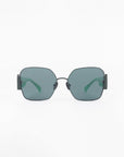 A pair of stylish, modern Frida Mask sunglasses from For Art's Sake® with black metal frames and dark green-tinted square lenses. The design features thin temples that curve inward slightly towards the ends, contrasting against the clear background. The ultra-lightweight nylon lenses offer 100% UVA & UVB protection.