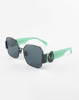 A pair of stylish **For Art's Sake® Frida Mask** sunglasses featuring black rectangular lenses with ultra-lightweight Nylon material and vibrant mint green frames. The temples are mint green with a decorative embellishment near the hinges, offering 100% UVA & UVB protection. The background is plain white.