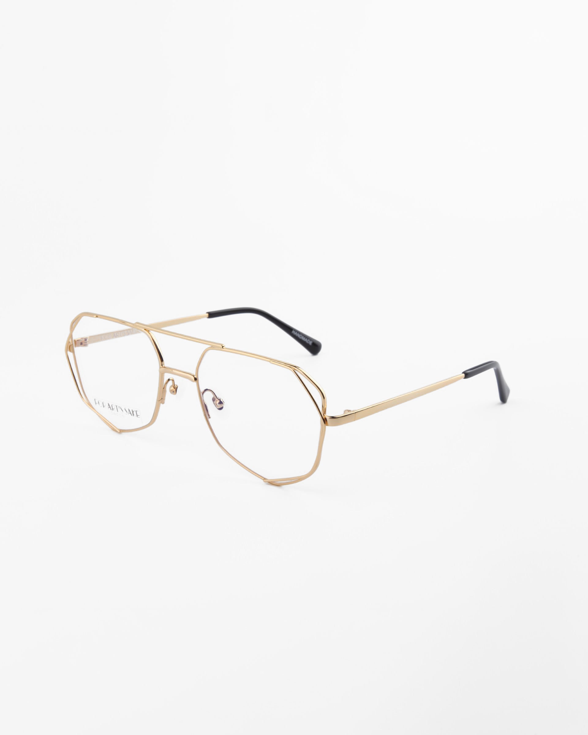 A pair of gold-framed eyeglasses with a thin, geometric design and clear lenses featuring UV protection. The temples have black tips, and the words &quot;For Art&#39;s Sake®&quot; are visible on one lens. The Genius Two glasses rest on a white background.