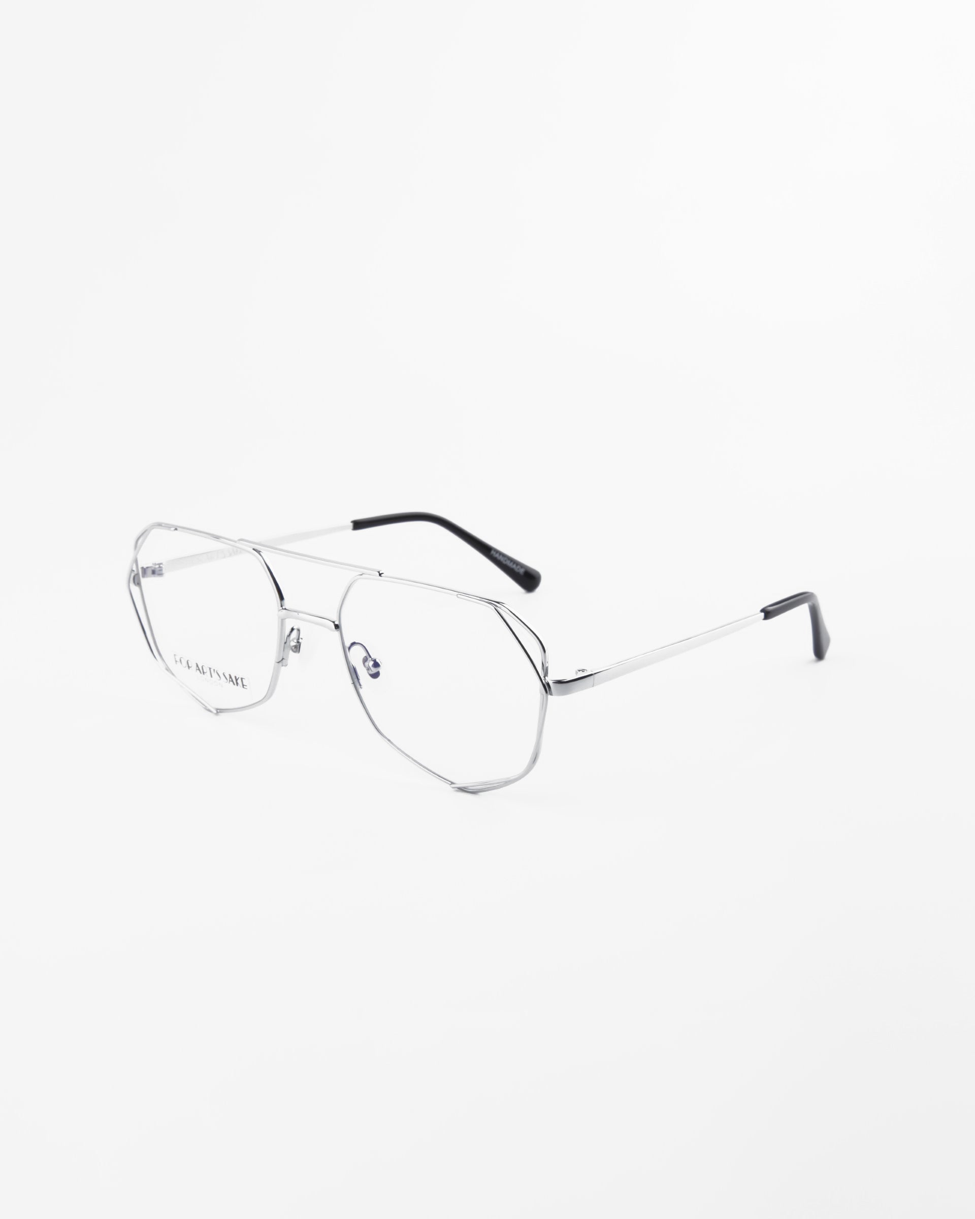 A pair of Genius Two by For Art&#39;s Sake® with thin, metallic frames and black tips on the arms is shown against a white background. The lenses are clear with a blue light filter, and the glasses have a modern, minimalist design. The frame brand name is visible on the left lens.