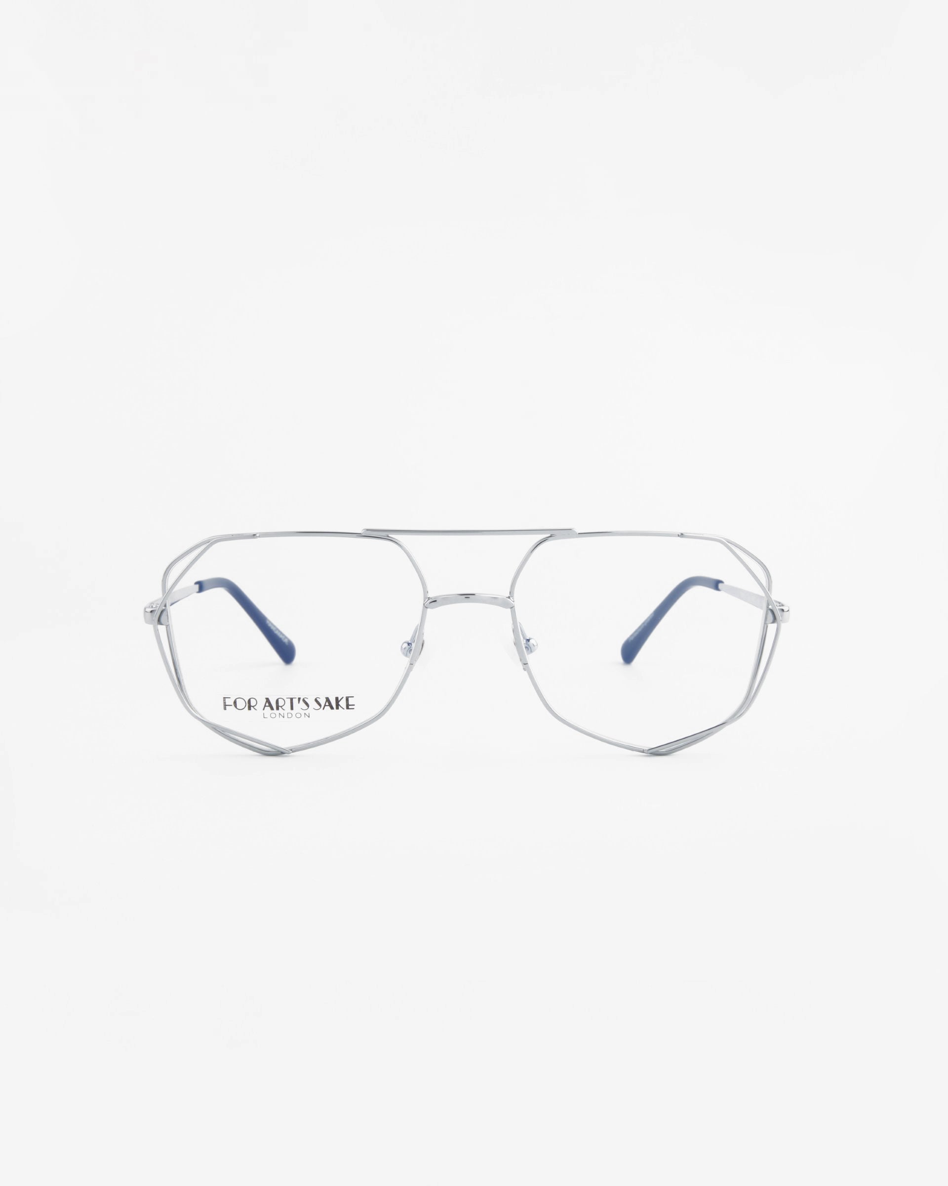 A pair of aviator-style eyeglasses with thin silver metal frames and navy blue temple tips. The lenses are clear with a built-in blue light filter, perfect for screen time. The left lens features the text &quot;FOR ART&#39;S SAKE.&quot; The background is a clean, solid white. These stylish eyeglasses are known as Genius Two by For Art&#39;s Sake®.