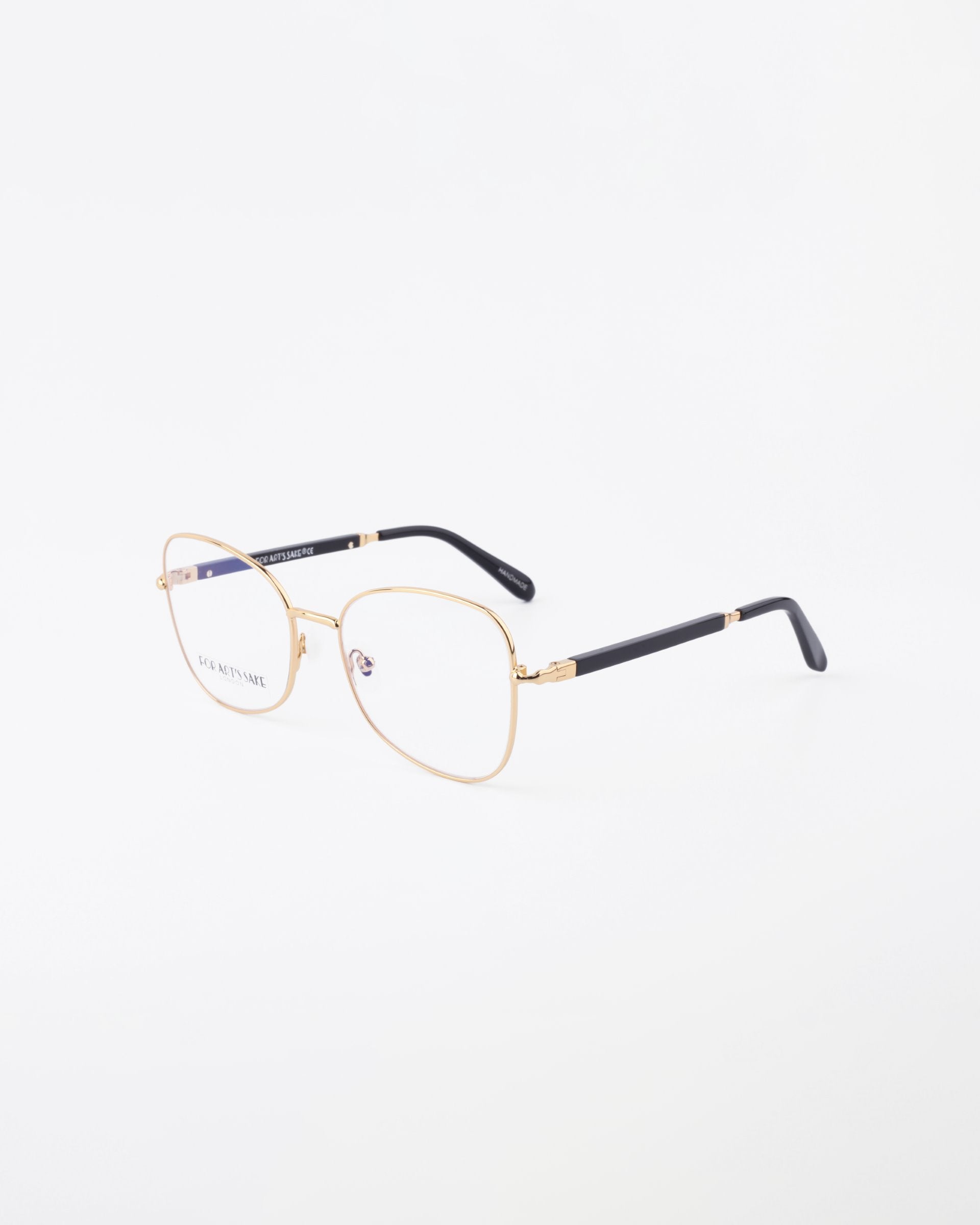 A pair of thin, 18-karat gold-plated eyeglasses displayed on a white background. The Grace glasses from For Art&#39;s Sake® have square lenses with black temple tips and small nose pads attached to the bridge for added comfort. One of the side arms is partially visible, showcasing a sleek black and gold design.