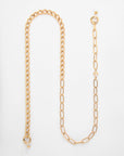 A For Art's Sake® Gabriel Glasses Chain crafted with 18K gold-plated links lies on a white surface. One side features tightly packed circular links, while the other side has larger, elongated rectangular links. Both ends have circular clasps, and one end is adorned with a small orb.