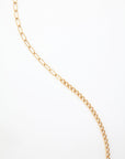 A For Art's Sake® Gabriel Glasses Chain displayed on a white background. The 18K gold-plated links vary in size, with larger oval links transitioning to smaller, more tightly connected circular links. The chain is arranged in a loose, wavy pattern across the background.