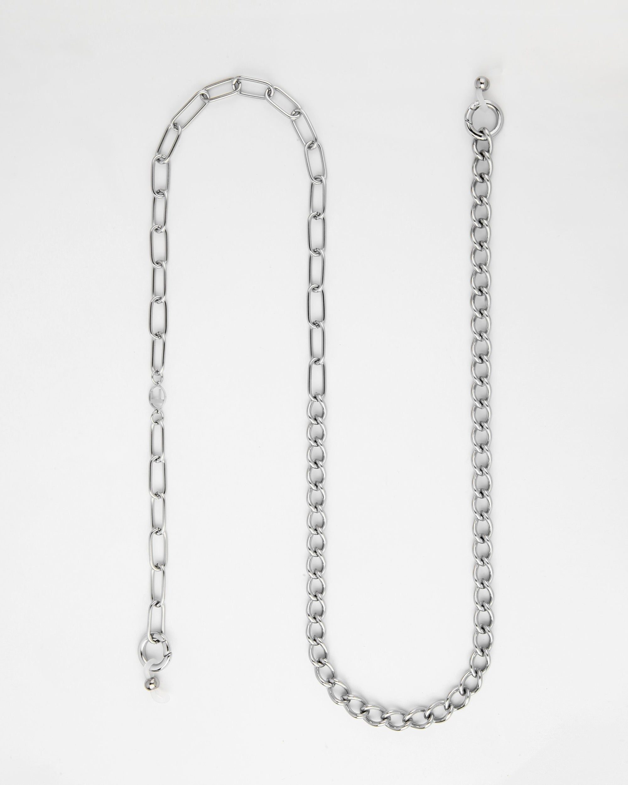 A silver Gabriel Glasses Chain by For Art's Sake® is laid out on a white background. The chain has a mix of different link styles, with one half featuring elongated links and the other half comprising denser, rounded links. There are two clasping mechanisms on either end.