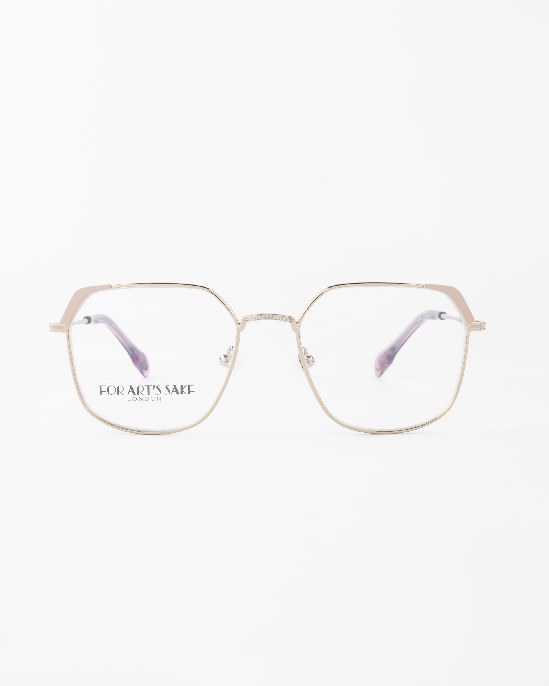 Close-up of gold-framed eyeglasses with hexagonal-shaped lenses and clear nose pads. The arms curve gracefully and feature a pale pink gradient. &quot;For Art&#39;s Sake®&quot; is printed on the left lens, offering both style and blue light filter for optimum eye comfort. The background is white.