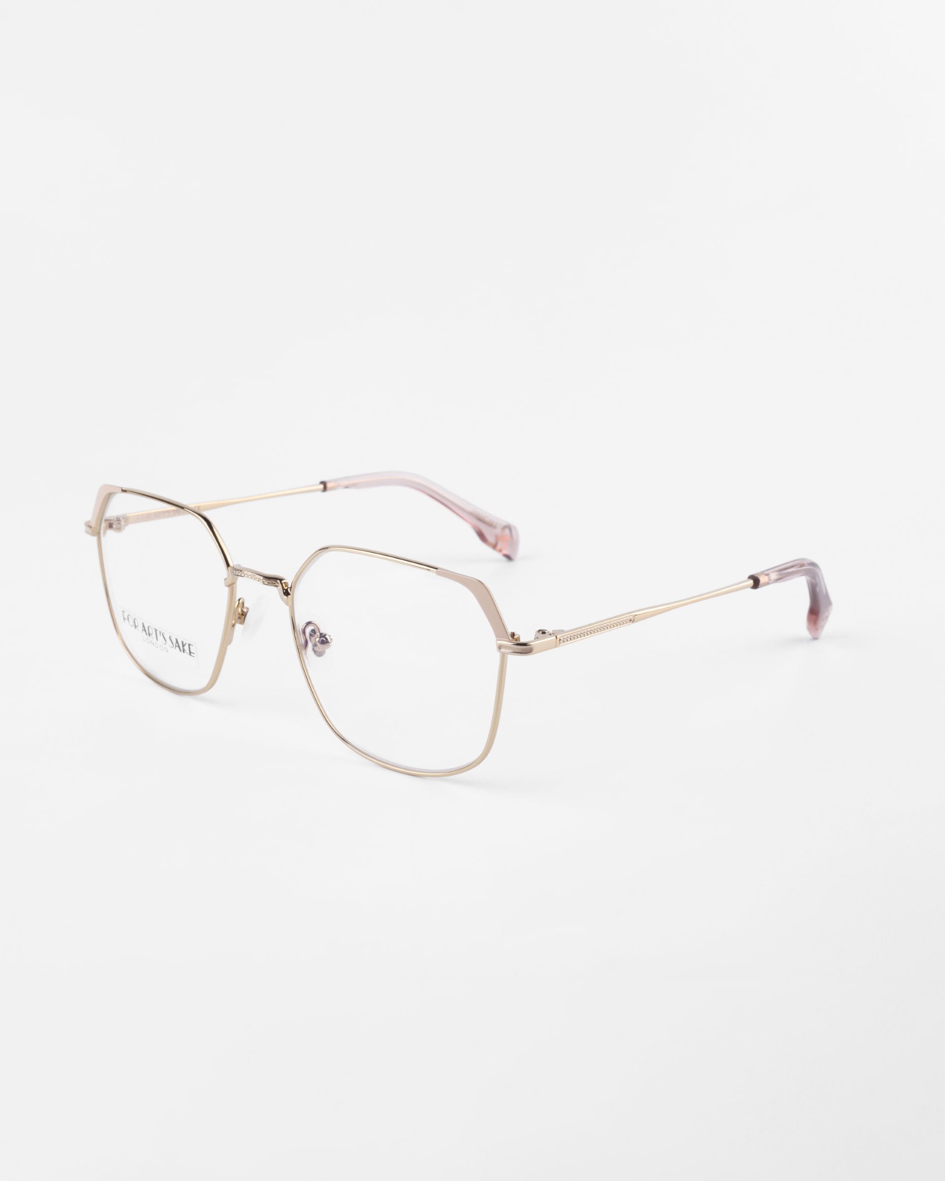 A pair of modern eyeglasses with thin, gold metal frames and clear prescription lenses featuring a blue light filter. The temples are straight with a subtle curve near the ends, which are covered with pinkish-brown tips. The white background highlights the sleek and minimalist design of the Godiva glasses by For Art's Sake®.
