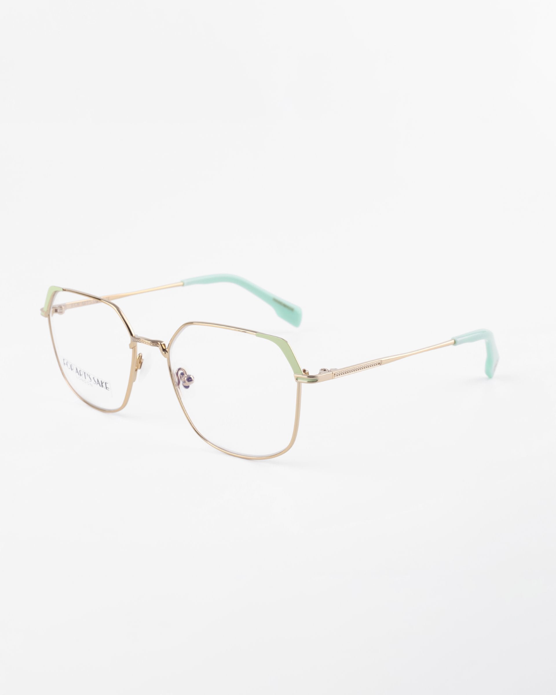 A pair of eyeglasses with gold wire frames and rectangular lenses, featuring mint green accents on the temples and end tips of the arms. These stylish glasses, named Godiva by For Art&#39;s Sake®, also come with optional prescription lenses. Displayed against a white background, they elegantly blend fashion with functionality.