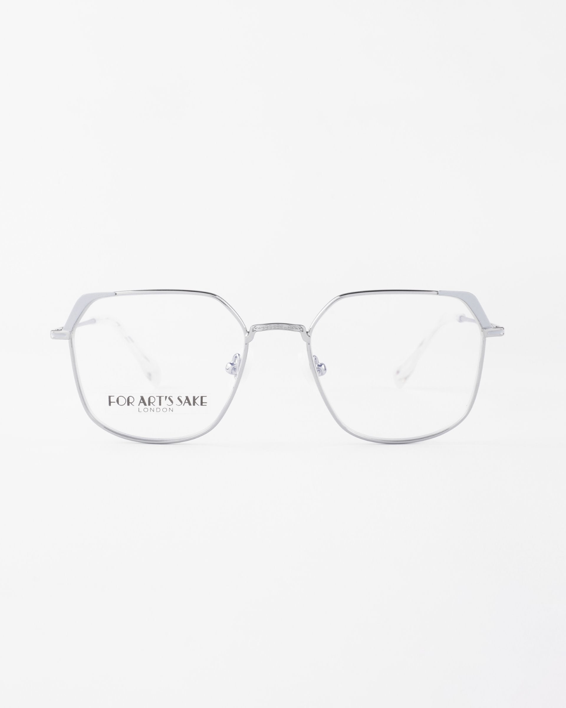 A pair of Godiva with metal frames and clear lenses featuring a blue light filter. The frames are thin and minimalist, with slightly rounded square shapes. The words &quot;FOR ART&#39;S SAKE LONDON&quot; are printed on the left lens. The background is plain white.