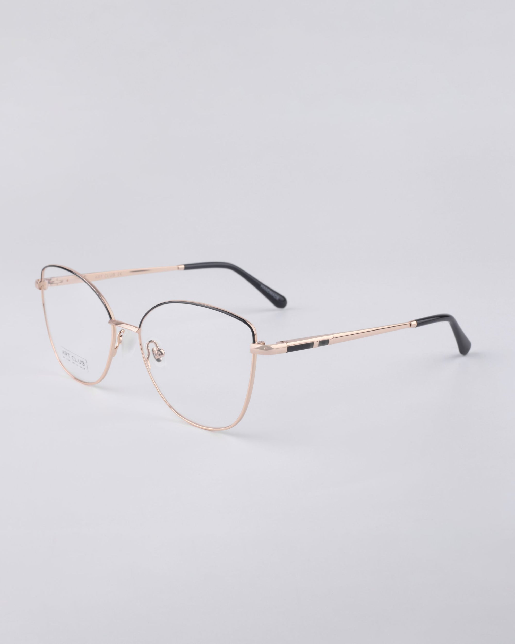 For Art's Sake® presents the Greta eyeglasses, featuring gold-finished rims with black temple tips against a light gray background. These modern frames offer a minimalist design and are equipped with blue light filter lenses, perfectly blending sustainable luxury with daily functionality.