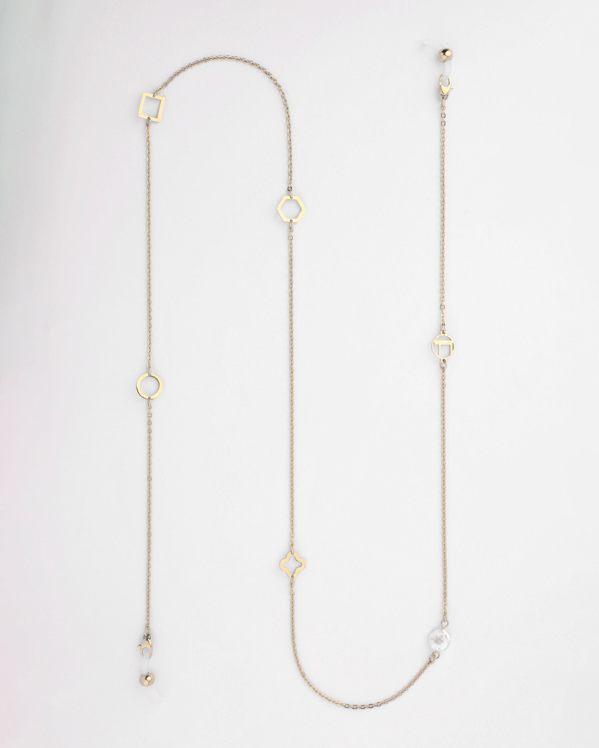 A long, delicate gold-plated necklace with a variety of small geometric charms including circles, squares, and a quatrefoil. This minimalistic piece also doubles as an elegant eyewear chain featuring pearl-like freshwater pearl embellishments. It is laid out against a plain white background. The Hampstead Glasses Chain by For Art's Sake® is the perfect blend of functionality and elegance.