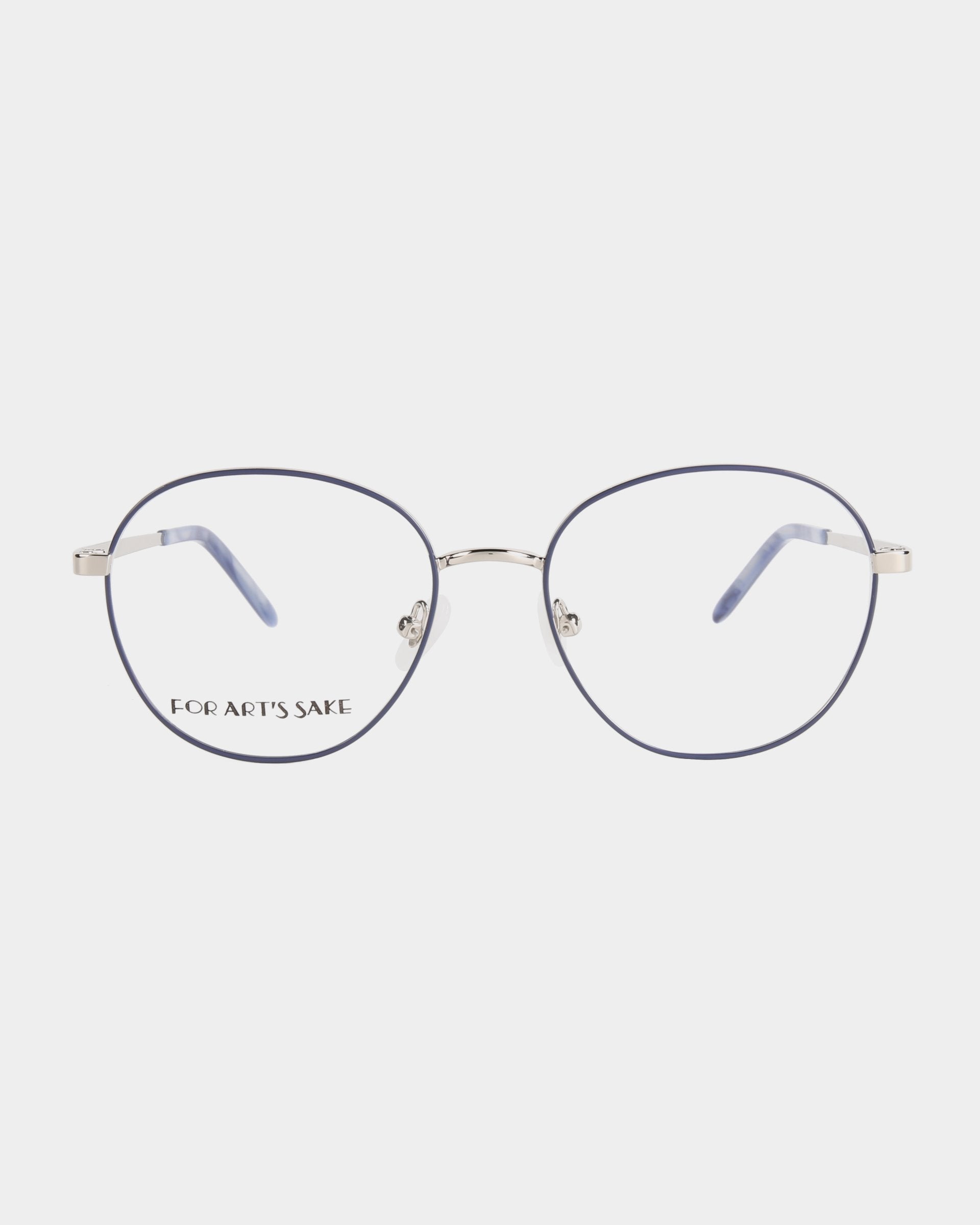 A pair of stylish eyeglasses with thin, silver metal frames and large round lenses. The temples are accented with a touch of blue on the tips. The left lens has "FOR ART'S SAKE" written in small, black font. Featuring adjustable nose pads and a blue light filter, the background is plain white. Product Name: Hailey Brand Name: For Art's Sake®