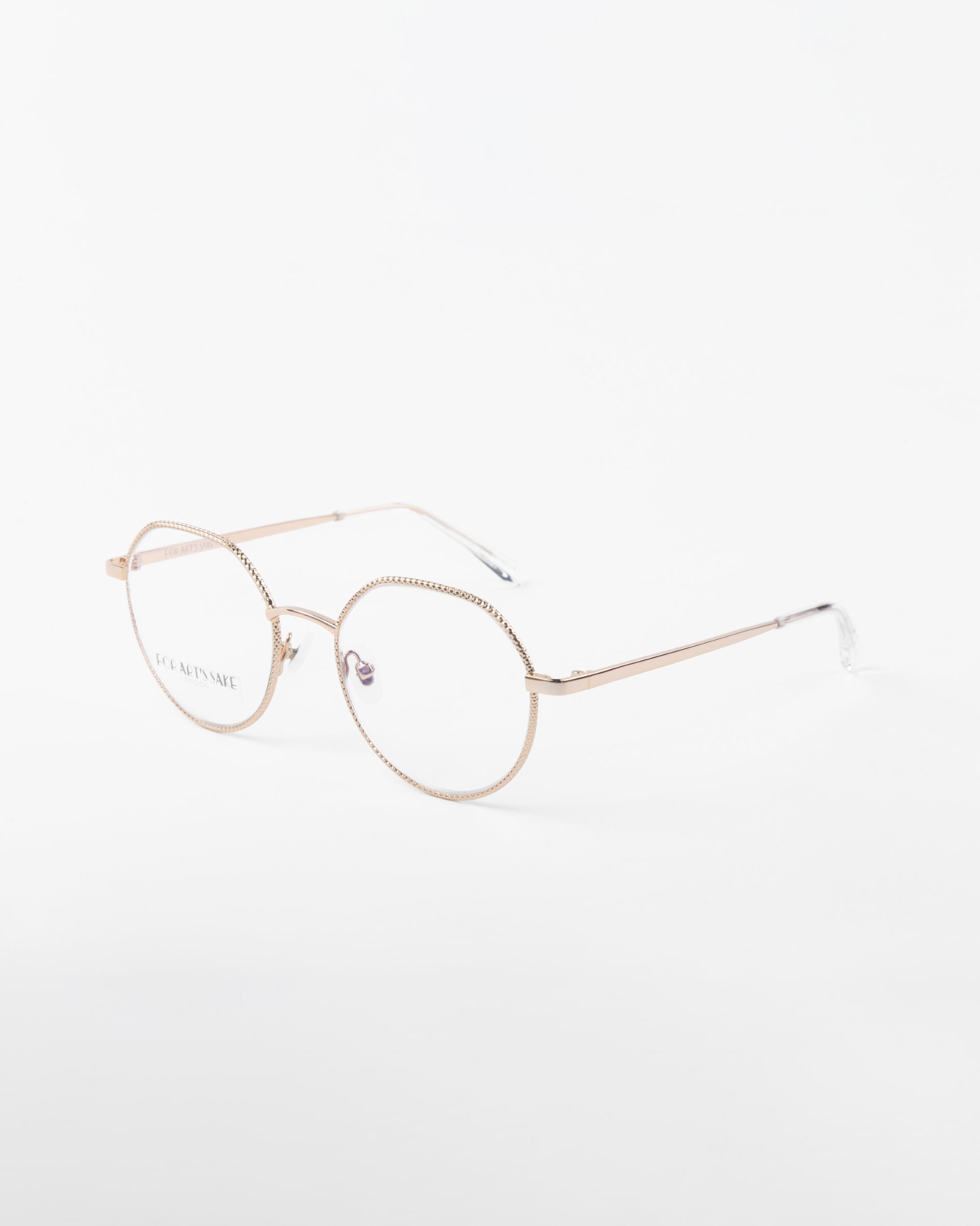 A pair of 18-karat gold-plated, round eyeglasses with clear lenses positioned at an angle against a white background. The frames have a thin, delicate design with a slight pattern on the rims. The temples are slender and straight with clear plastic tips. Perfect for adding blue light filter or prescription service! These are the Hope eyeglasses by For Art's Sake®.