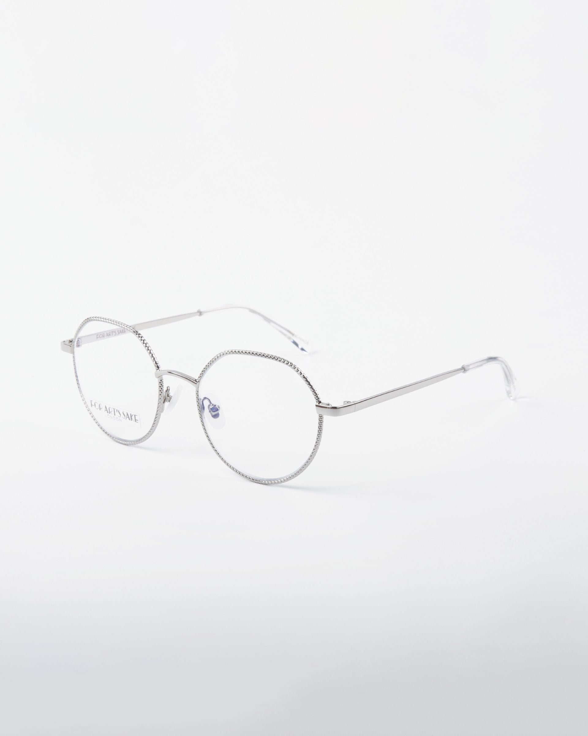 A pair of Hope eyeglasses by For Art&#39;s Sake® with round lenses and thin, 18-karat gold-plated arms. The frame features a subtle textured pattern around the lenses. The background is plain white, making the eyeglasses the focal point of the image.