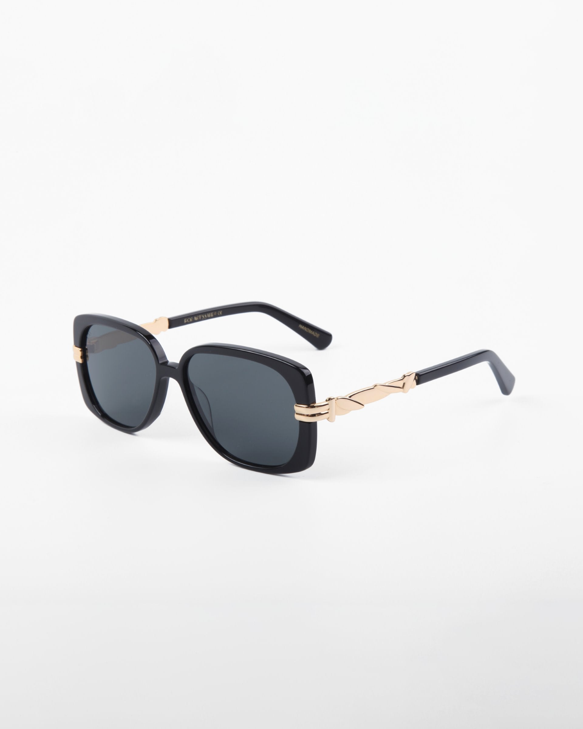 A pair of black square-framed Icon sunglasses by For Art&#39;s Sake® with dark, shatter-resistant nylon lenses. The temples feature gold accents near the hinges. Offering UVA &amp; UVB protection, they are perfect for sunny days. The background is plain and white.