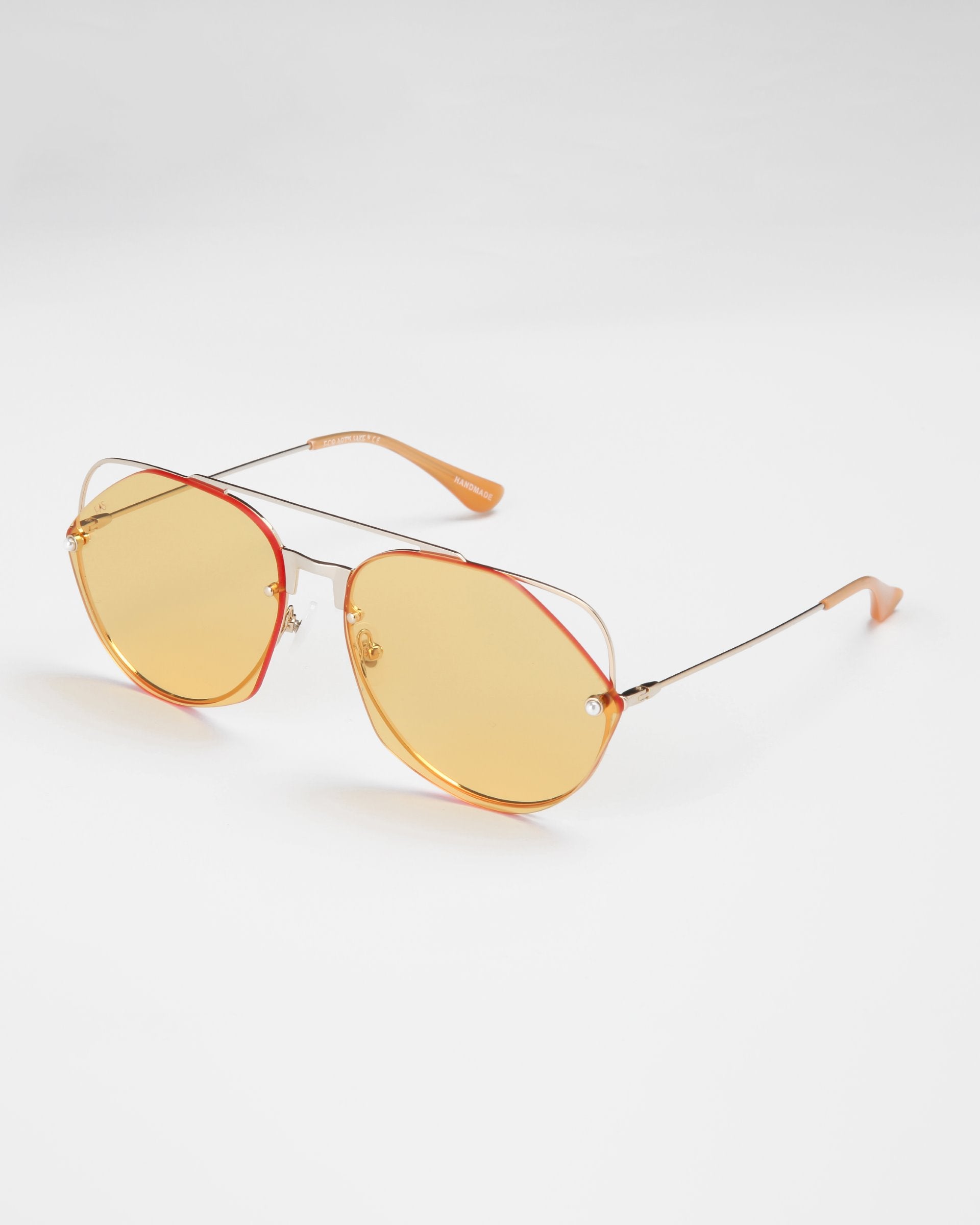 A pair of stylish For Art's Sake® Casino sunglasses with large, hexagonal-shaped yellow nylon lenses offering UV protection, thin gold metal frames, and orange-tipped arms. The sunglasses are placed on a plain white background.