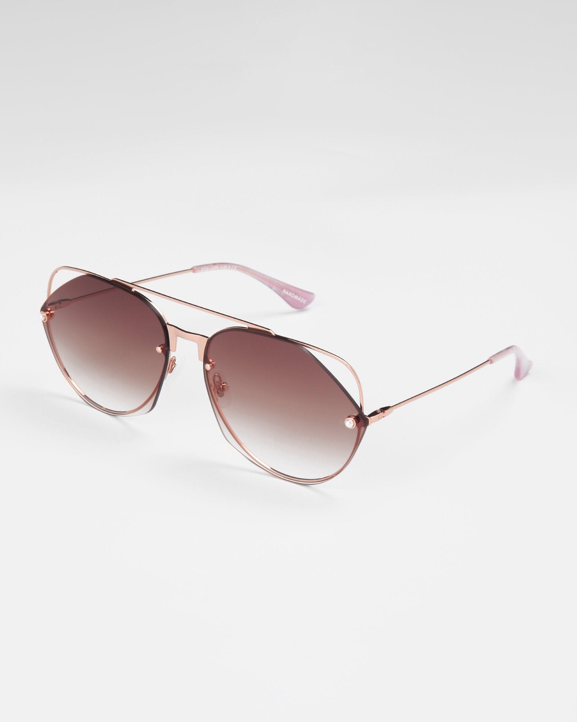 A pair of stylish For Art&#39;s Sake® Casino sunglasses featuring pink-tinted nylon lenses and rose gold metal frames. The temples are slim and extend to pink plastic ear tips, adding a slight feminine touch. Offering UV protection, the sunglasses are displayed against a plain white background.