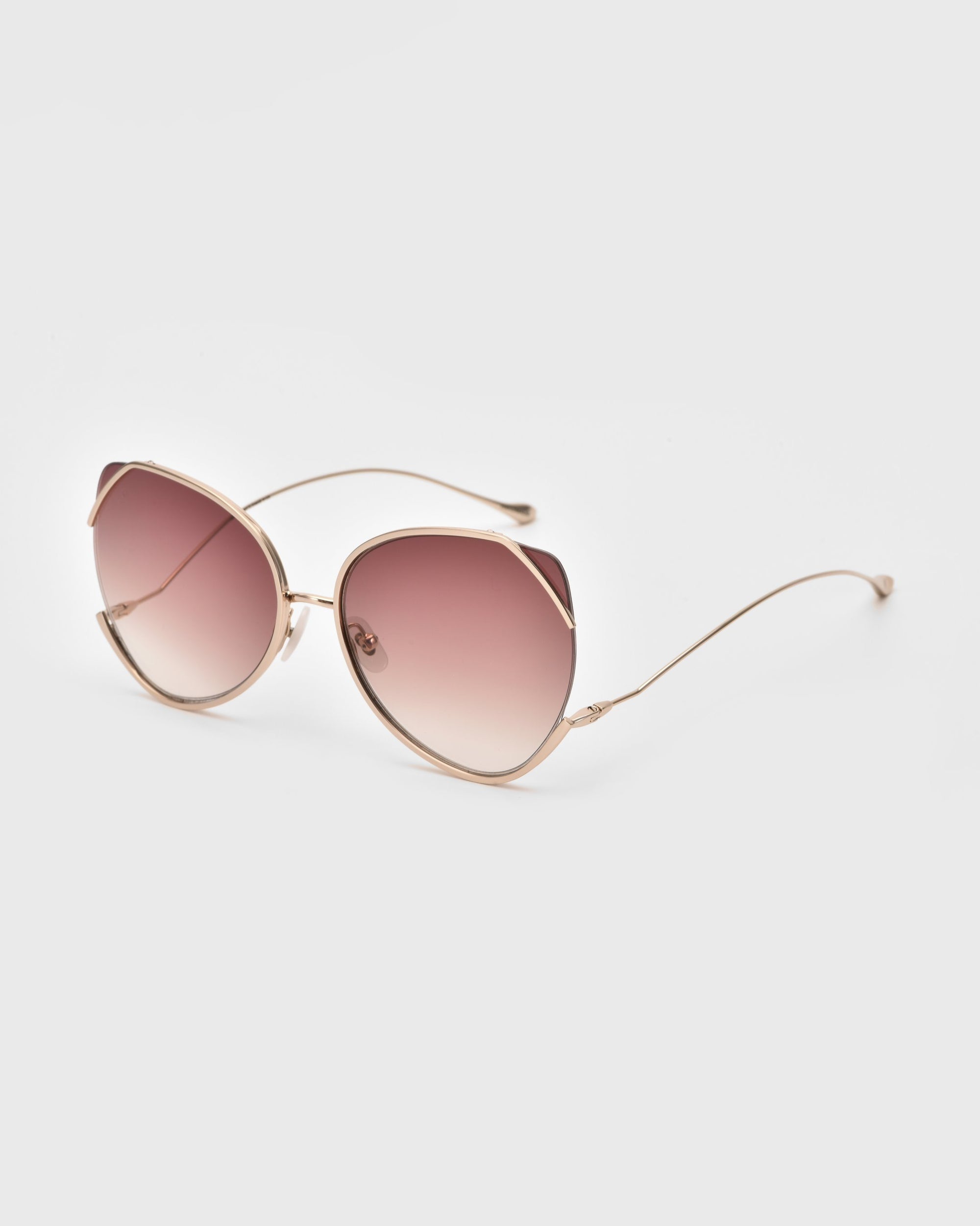 A pair of stylish For Art&#39;s Sake® Wonderland sunglasses with gold metal frames, highlighted by large, rounded lenses featuring a gradient tint from dark pink to light pink. Perfectly crafted with UV protection and adorned with jadestone nose pads, they rest elegantly on a white background.