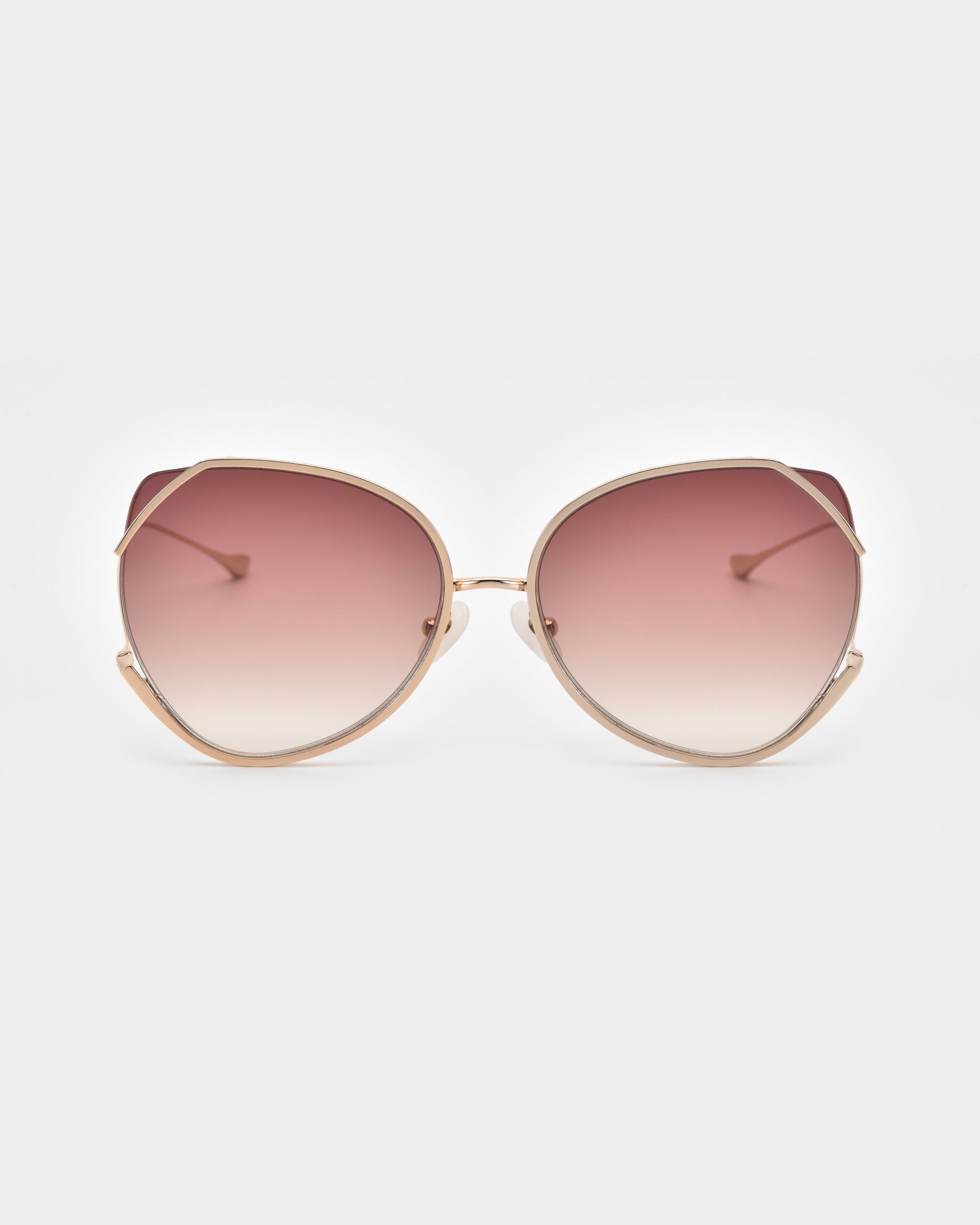 A pair of Wonderland by For Art&#39;s Sake® stylish sunglasses with large, round lenses that transition from pink at the top to clear at the bottom. Featuring jadestone nose pads for comfort and UV protection, these sunglasses have a thin, gold metal frame and slightly curved temples, all set against a plain white background.