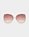 A pair of Wonderland by For Art's Sake® stylish sunglasses with large, round lenses that transition from pink at the top to clear at the bottom. Featuring jadestone nose pads for comfort and UV protection, these sunglasses have a thin, gold metal frame and slightly curved temples, all set against a plain white background.