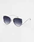 A pair of stylish Wonderland sunglasses by For Art's Sake® featuring sleek, thin, silver frames and large, slightly cat-eye shaped lenses with a gradient tint from dark gray to transparent. The minimalist design is modern and elegant, with delicate jadestone nose pads and ultralightweight lenses offering 100% UV protection.