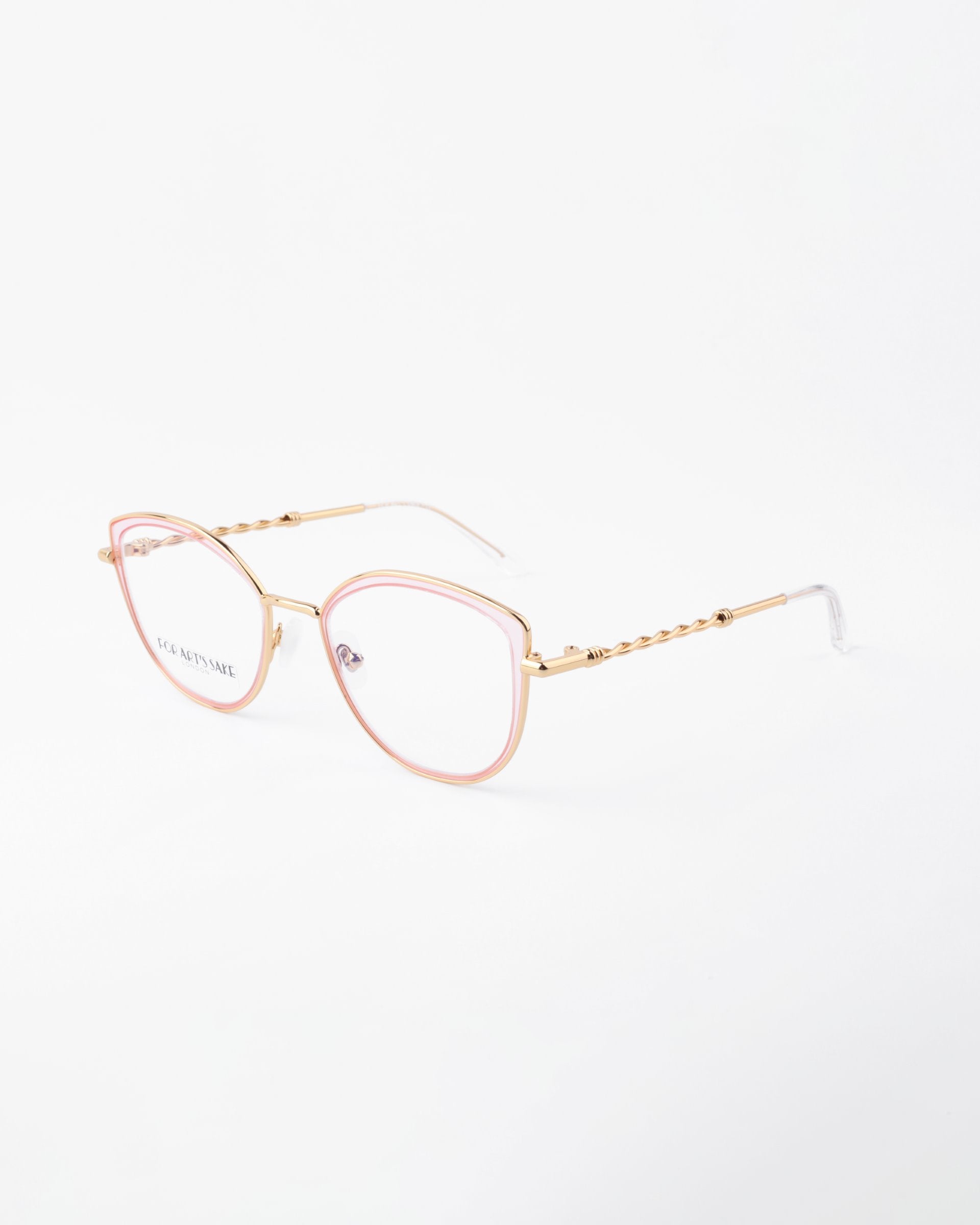 A pair of eyeglasses with gold-colored, thin, metal frames and pink accents around the lenses. The temples feature a decorative pattern and clear, adjustable nose pads. These 18-karat gold-plated glasses are displayed against a plain white background. They are the Julie by For Art&#39;s Sake®.