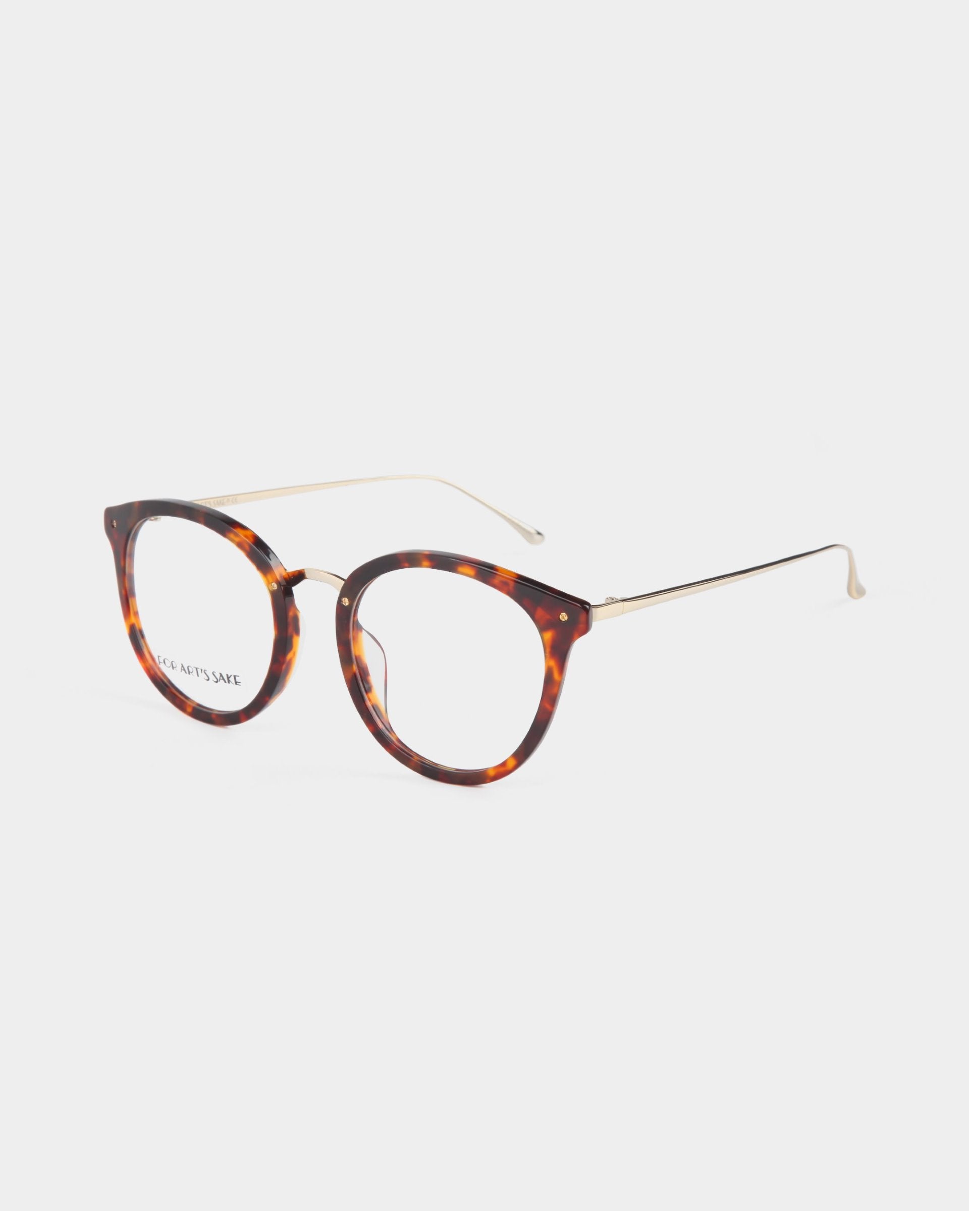 A pair of Jackie eyeglasses by For Art's Sake® with round tortoiseshell frames and slender gold metal temples. The tips of the temples are curved slightly for a comfortable fit. Featuring UV protection lenses, a small logo is visible on one lens. The overall design is stylish and modern.