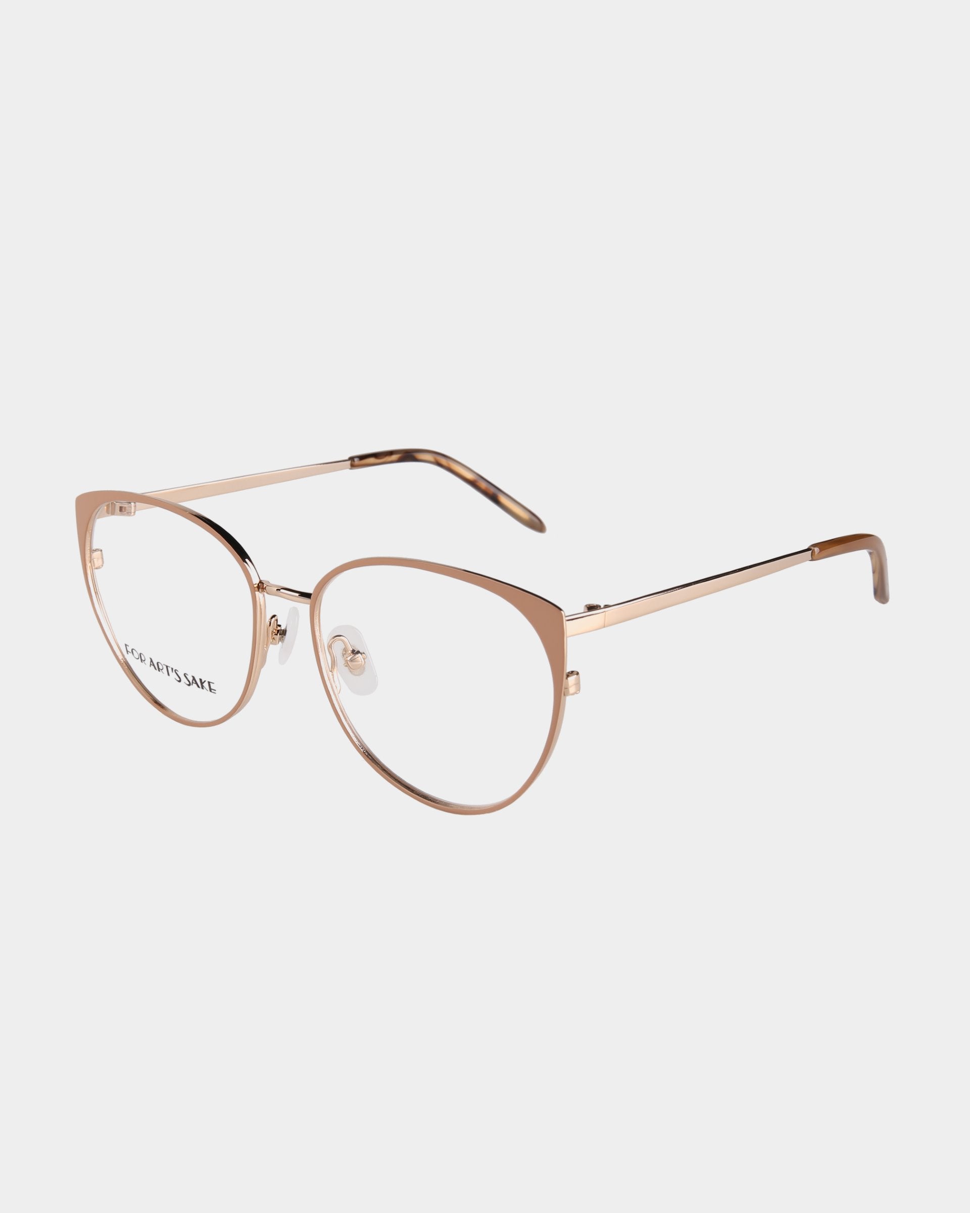 A pair of elegant, rose gold eyeglasses with a sleek and modern cat-eye frame design. Featuring 18-karat gold plating, the Kaia glasses by For Art's Sake® have thin metal arms and clear lenses, suitable for both fashion and functionality. The lightweight frame includes subtle, stylish detailing.