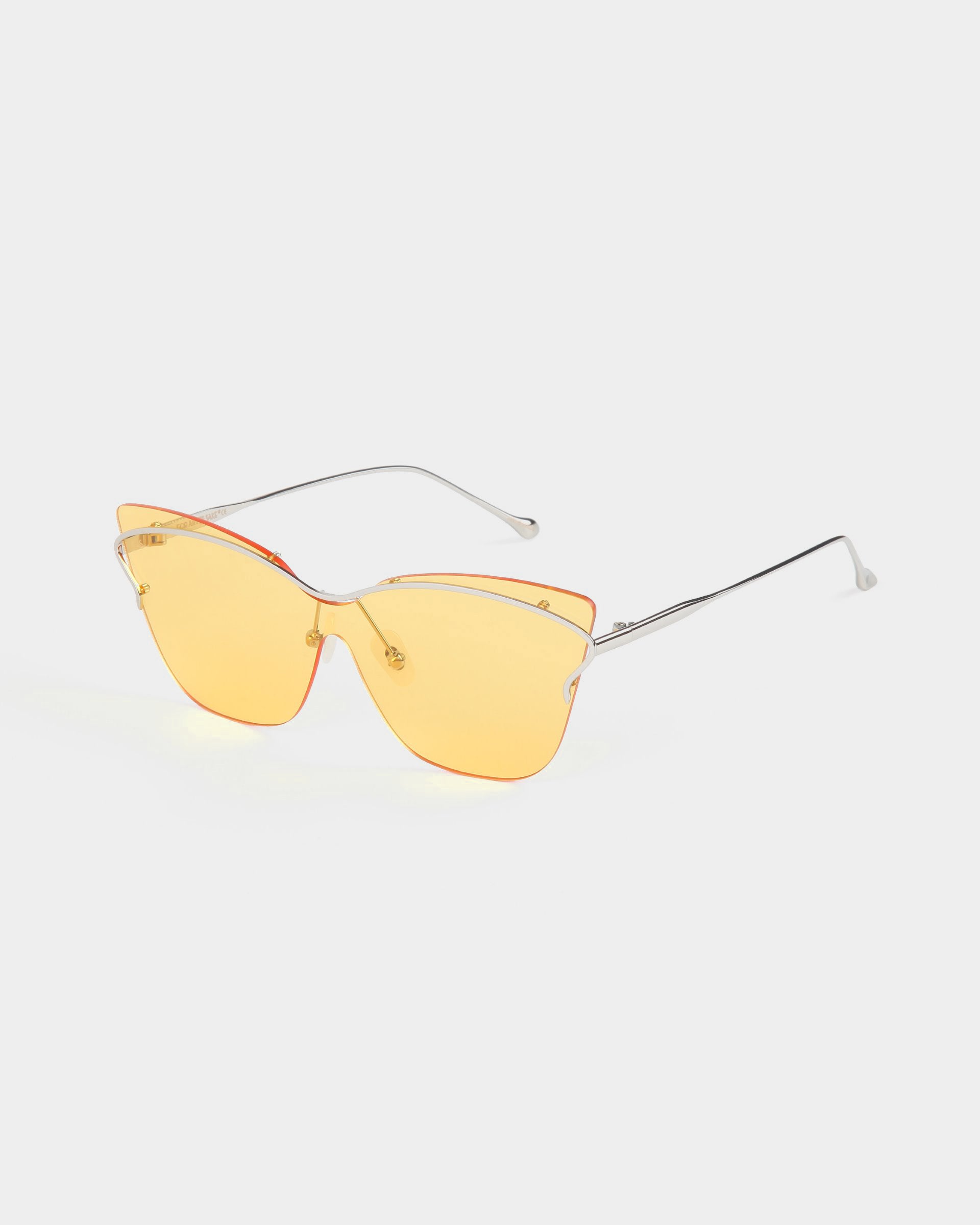 The Kelly sunglasses by For Art&#39;s Sake® feature stylish eyewear with yellow-tinted, butterfly-shaped lenses. The glasses boast thin metal arms with a slight curve at the ends. With their rimless design, these retro-futuristic sunglasses offer a modern, minimalist appearance against a plain, light gray background.