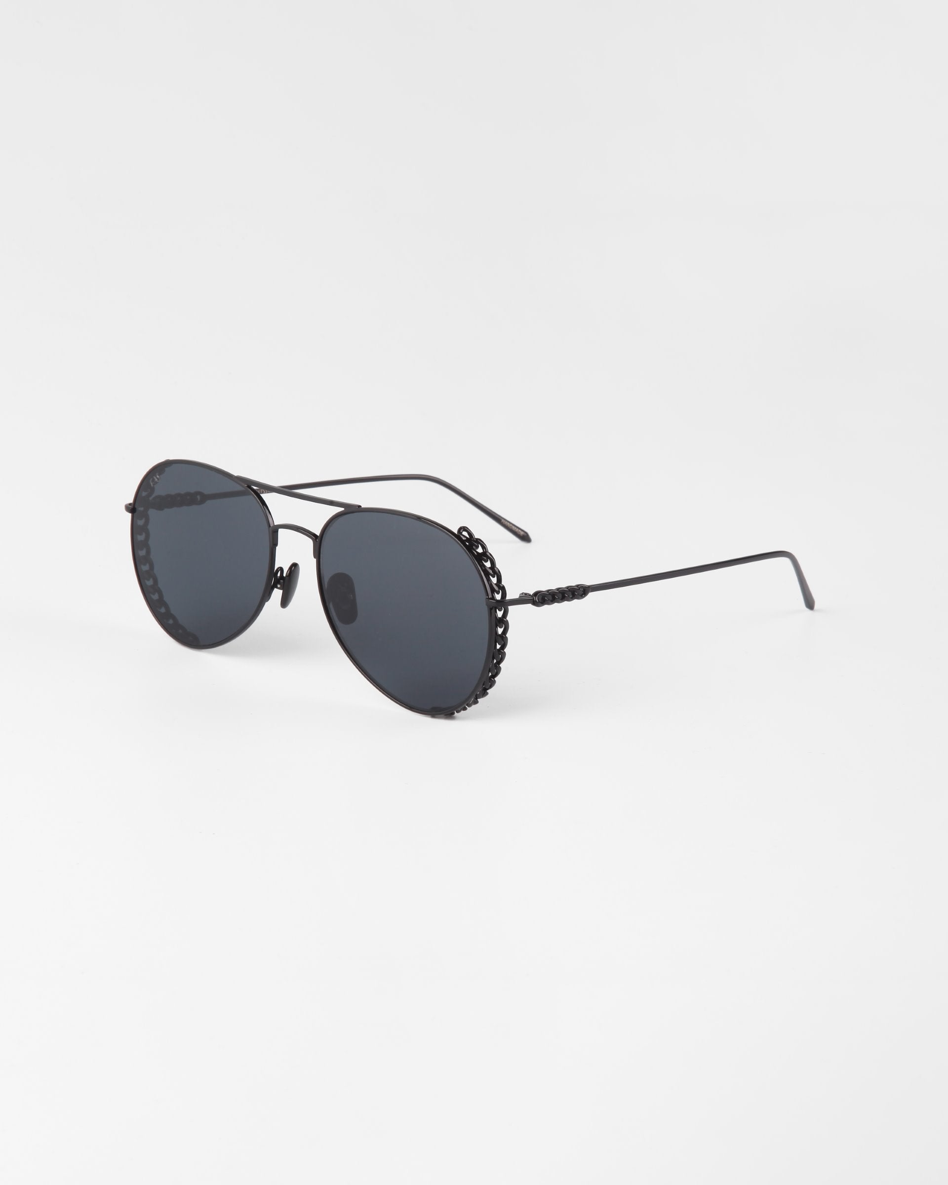 A pair of stylish black aviator sunglasses with dark nylon lenses, named Links by For Art&#39;s Sake®. The thin, gold-plated stainless steel frames are ornate, featuring intricate detailing on the sides. Placed on a plain white background and angled slightly to the left, they exude an air of elegance.