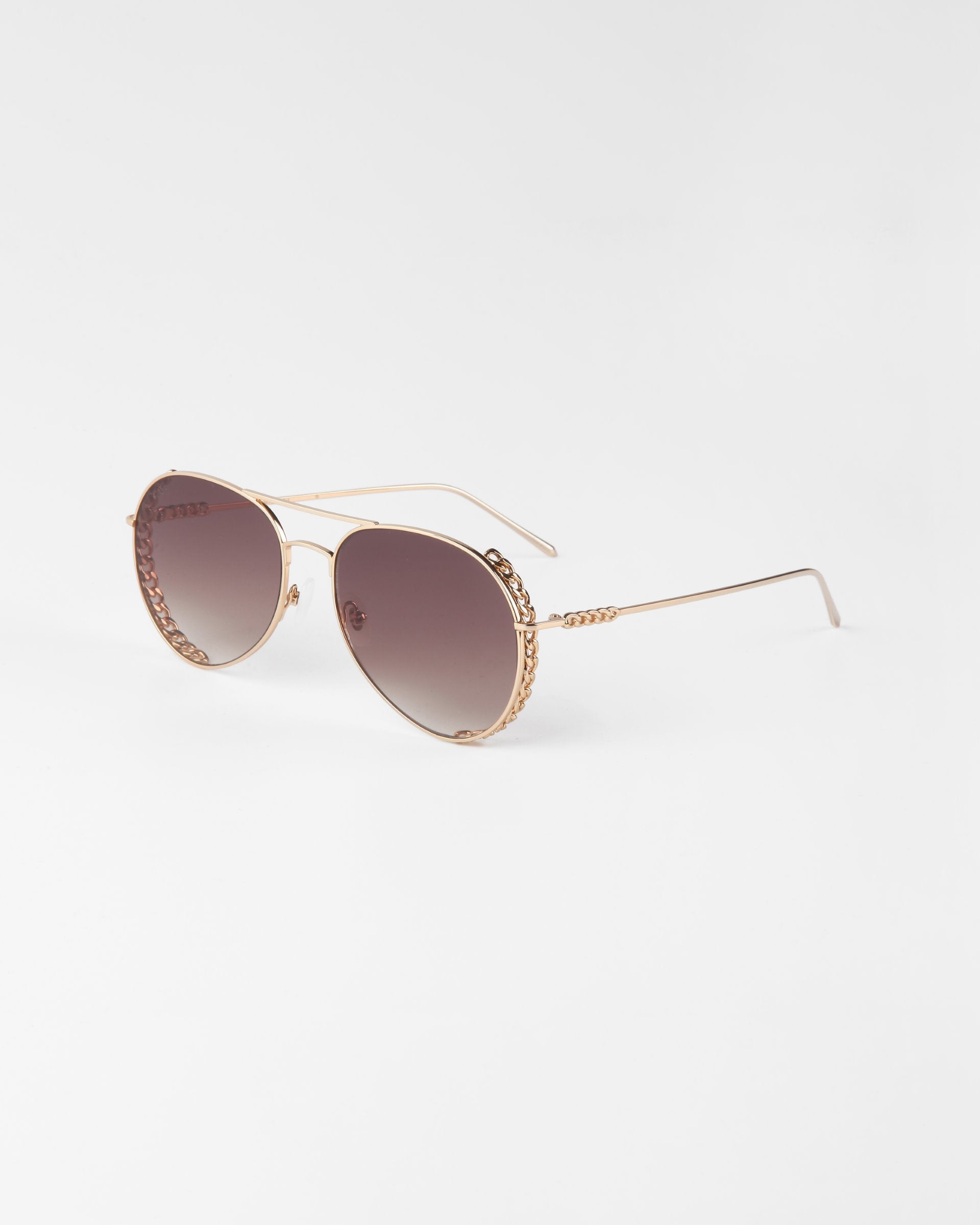 A pair of Links sunglasses by For Art&#39;s Sake® with gold-plated stainless steel frames and gradient brown nylon lenses, showcased on a white background. The sunglasses feature a braided detail on the brow bar and temple tips.