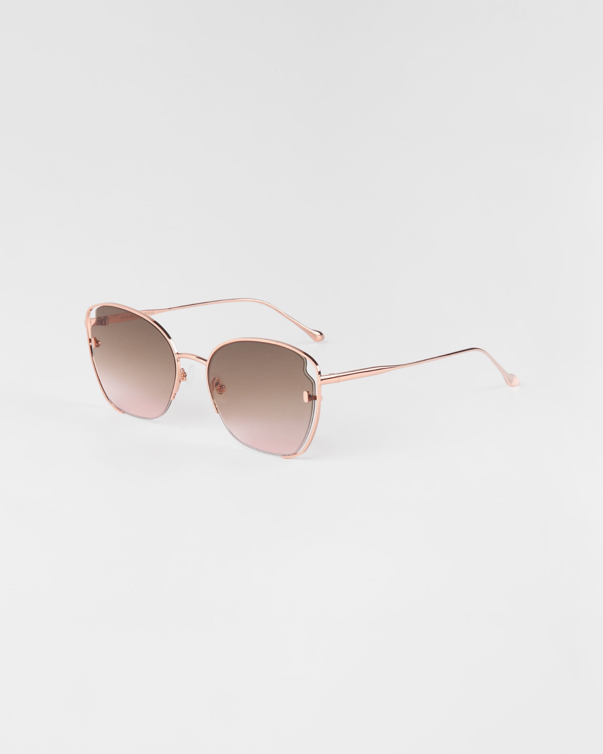 A pair of stylish For Art's Sake® Eden sunglasses, 18-karat gold plated with a thin metal frame and gradient lenses. The design features a slight cat-eye shape and sleek temples, offering UVA & UVB protection as they cast a soft shadow on the white background.