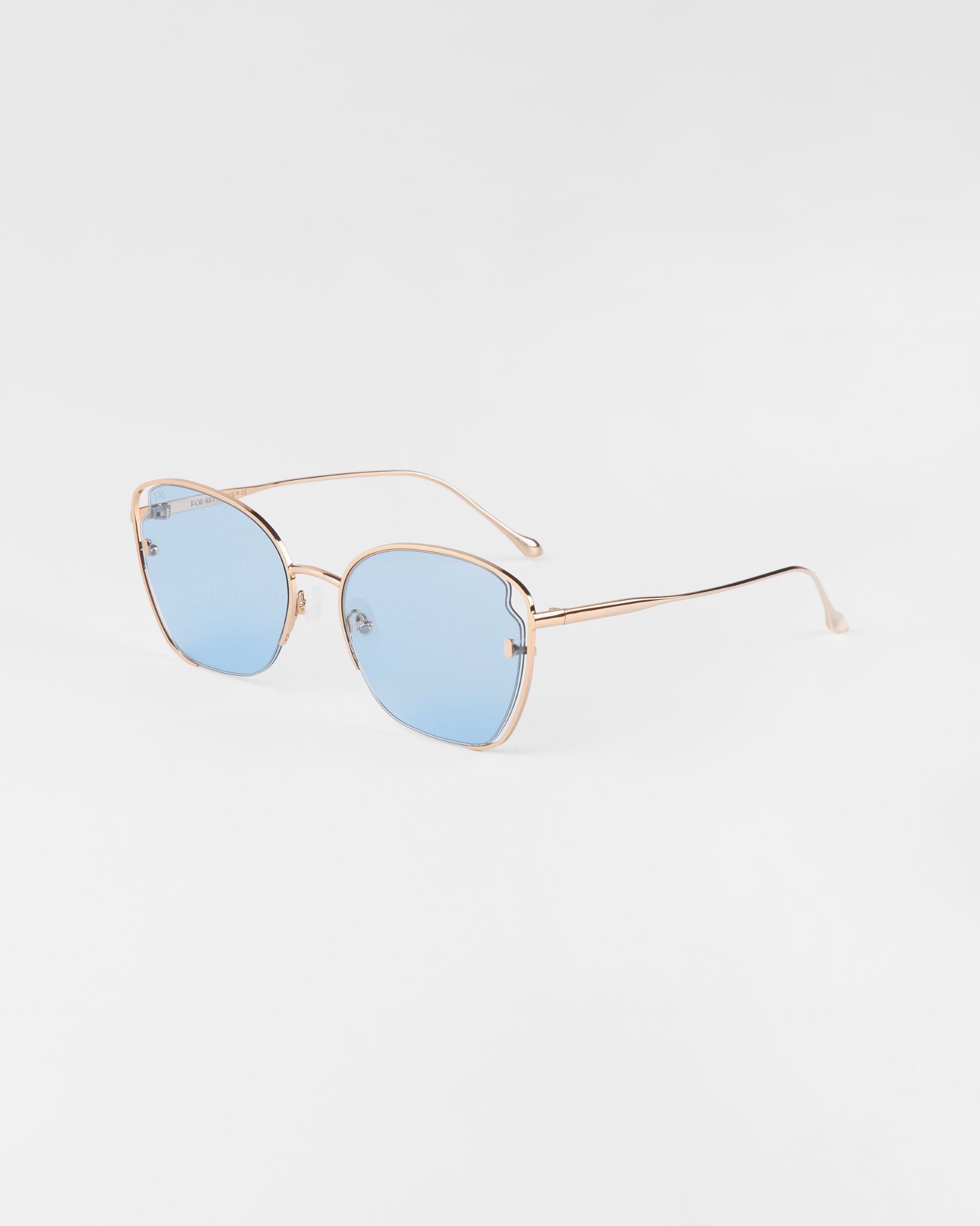 A pair of Eden sunglasses by For Art&#39;s Sake® with thin, 18-karat gold-plated frames and light blue-tinted square lenses is displayed against a plain white background. The glasses have subtly curved arms and a minimalist design, exuding a modern and sophisticated appearance, while being UVA &amp; UVB-protected.