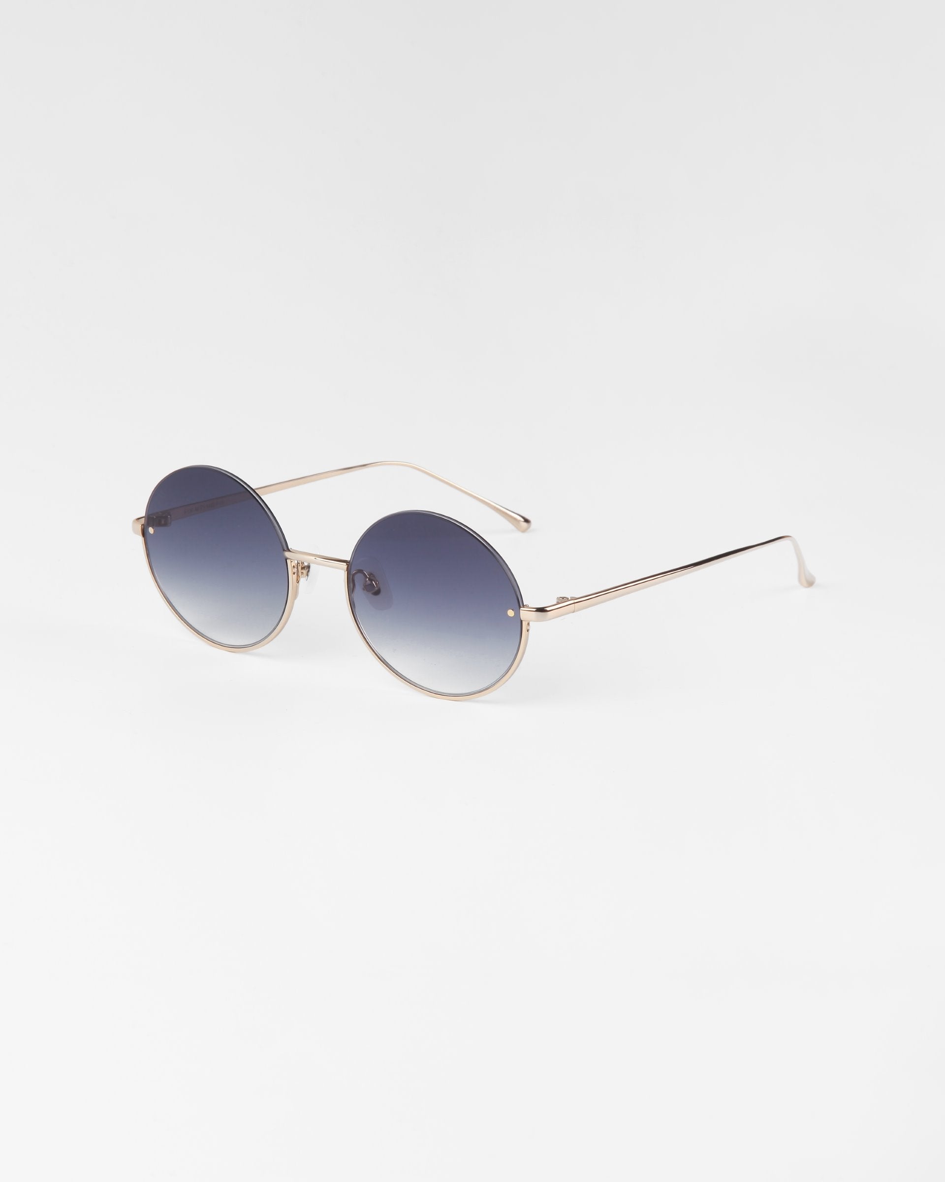 Skyline sunglasses by For Art&#39;s Sake® with 18-karat gold plated frames and gradient blue-tinted lenses. The thin arms of the glasses match the luxurious gold frame, creating a stylish and modern look. The background is a plain white surface.