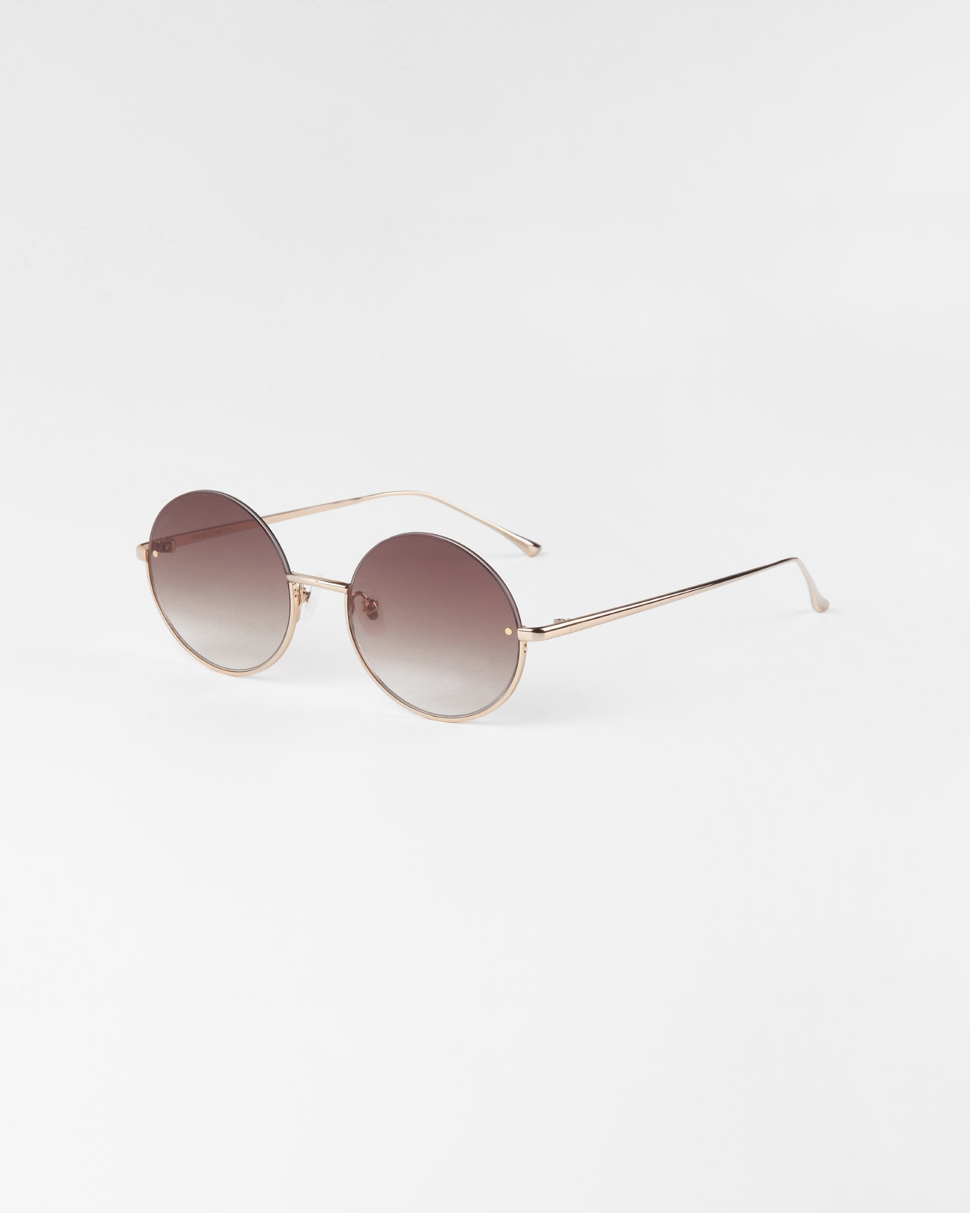 A pair of round sunglasses with thin 18-karat gold plated frames and brown gradient lenses is displayed against a plain white background. The Skyline by For Art&#39;s Sake® features a minimalist design with straight arms and nose pads for comfort.
