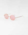 A pair of Skyline by For Art's Sake® round, pink-tinted sunglasses with slim, 18-karat gold-plated frames and temples. The minimalistic design features thin nose pads and lightweight construction with nylon lenses, all set against a plain white background.