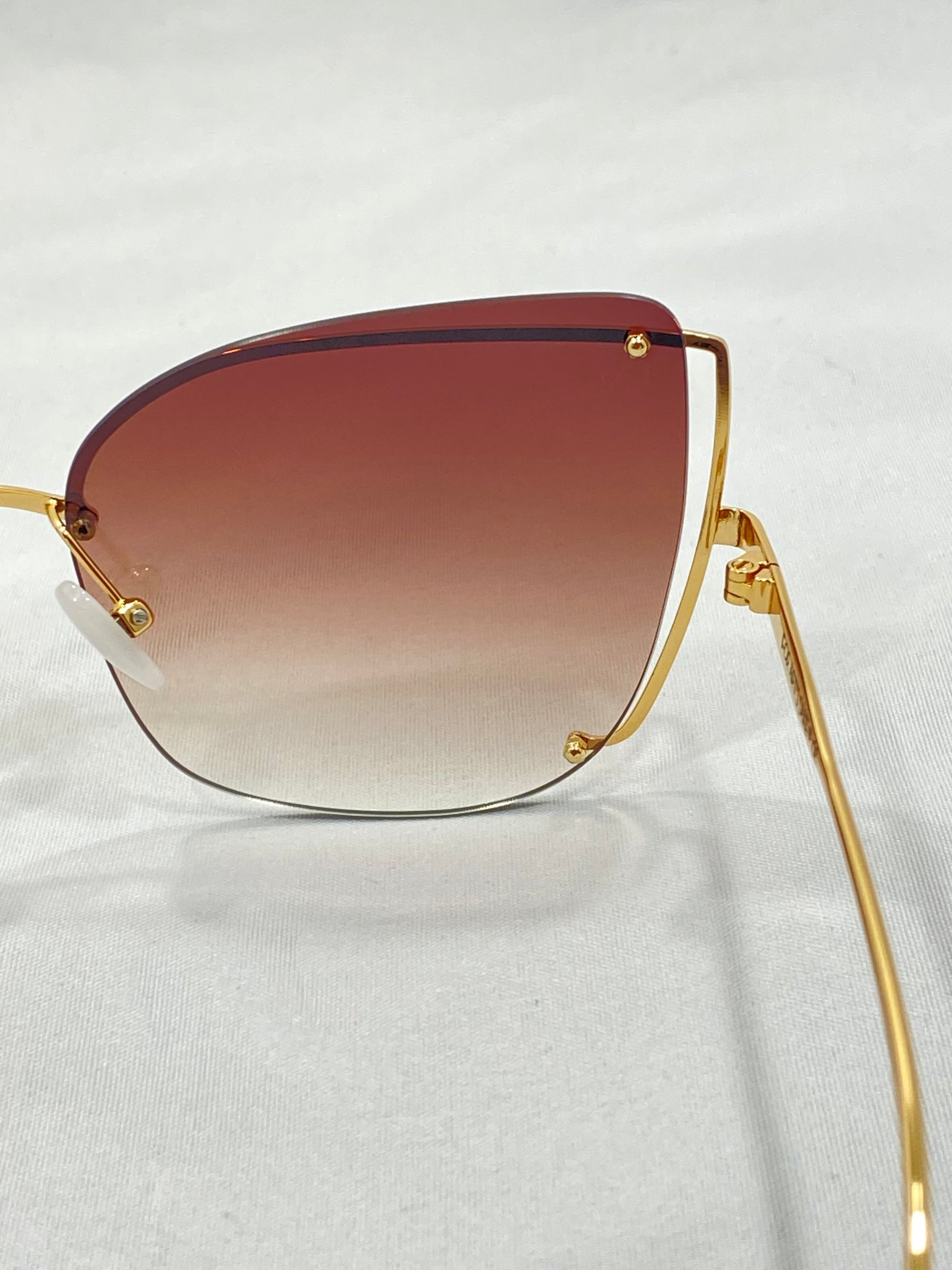 Close-up image of stylish Meow sunglasses by For Art&#39;s Sake® featuring gradient brown lenses and a gold wireframe. The lenses have a unique triangular shape with rounded edges, reminiscent of a cat-eye silhouette, and the frame is thin with minimalistic detailing, creating a sleek and modern look.